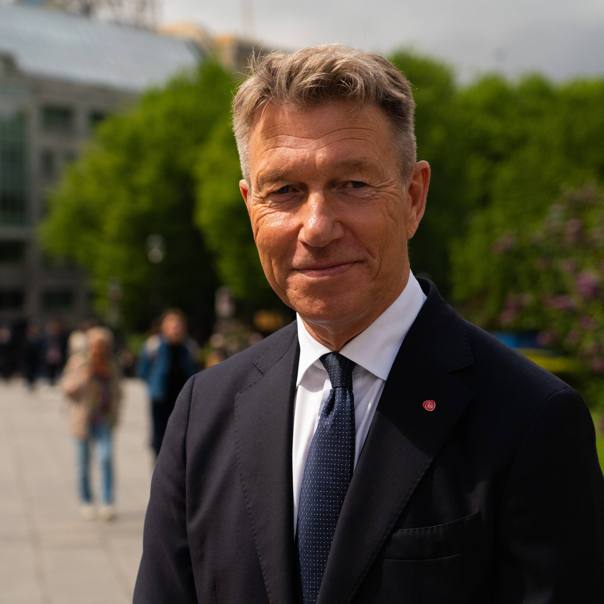 Portrett av Terje Aasland, energiminister. Står utendørs i bybildet. Trær og mennesker er uskarpe i bakgrunnen. Det er sol og han smiler. 