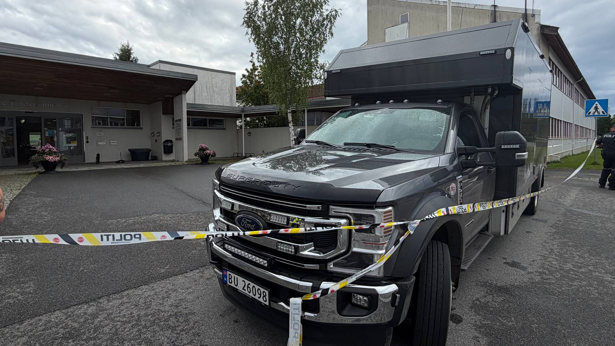 En politibil er sperret av med politibånd foran en offentlig bygning. 