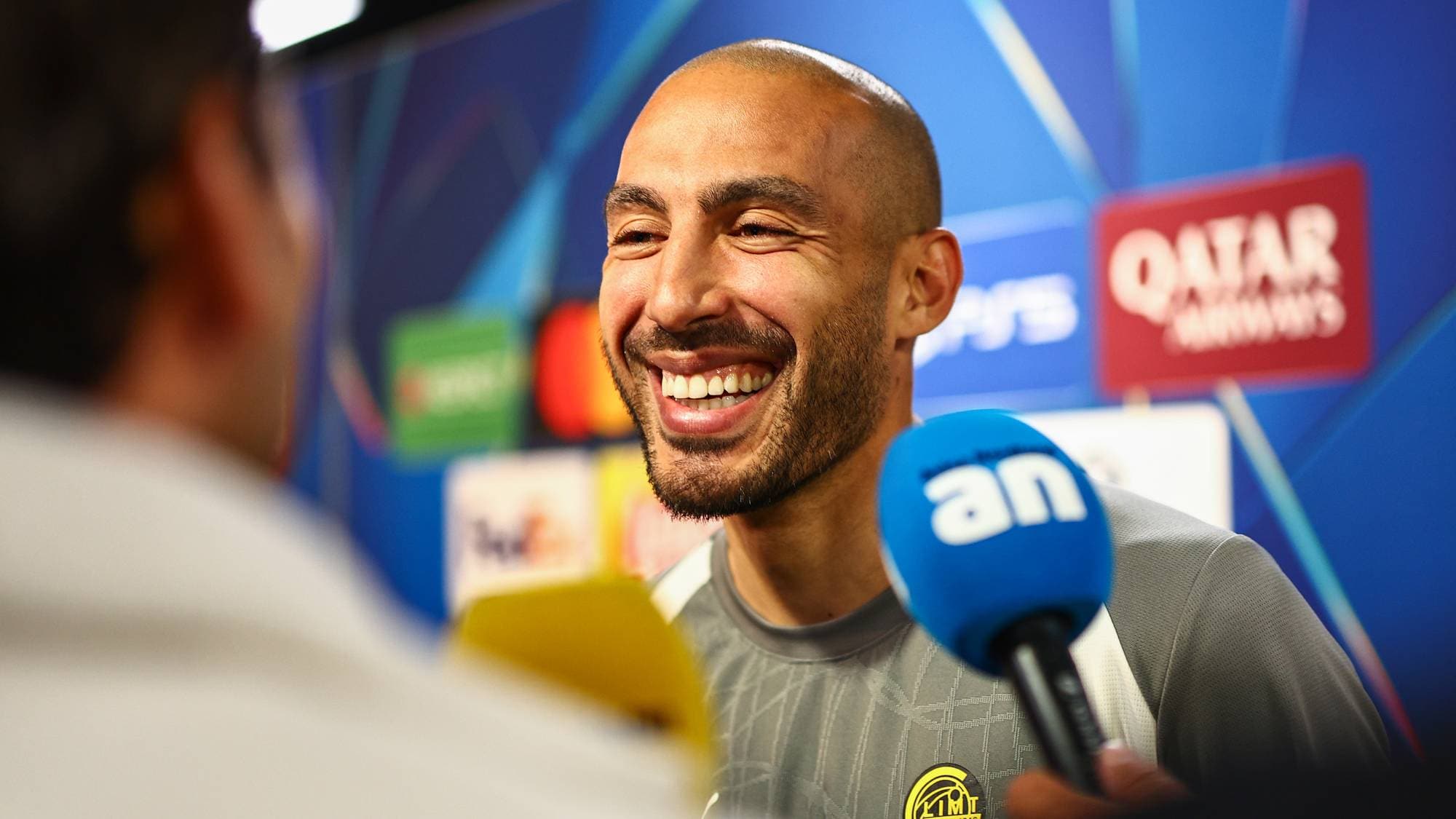 Fotballspilleren Omar Elabdellaoui smiler under et intervju med mikrofoner foran seg. (Bildebeskrivelsen er laget av en KI-tjeneste)