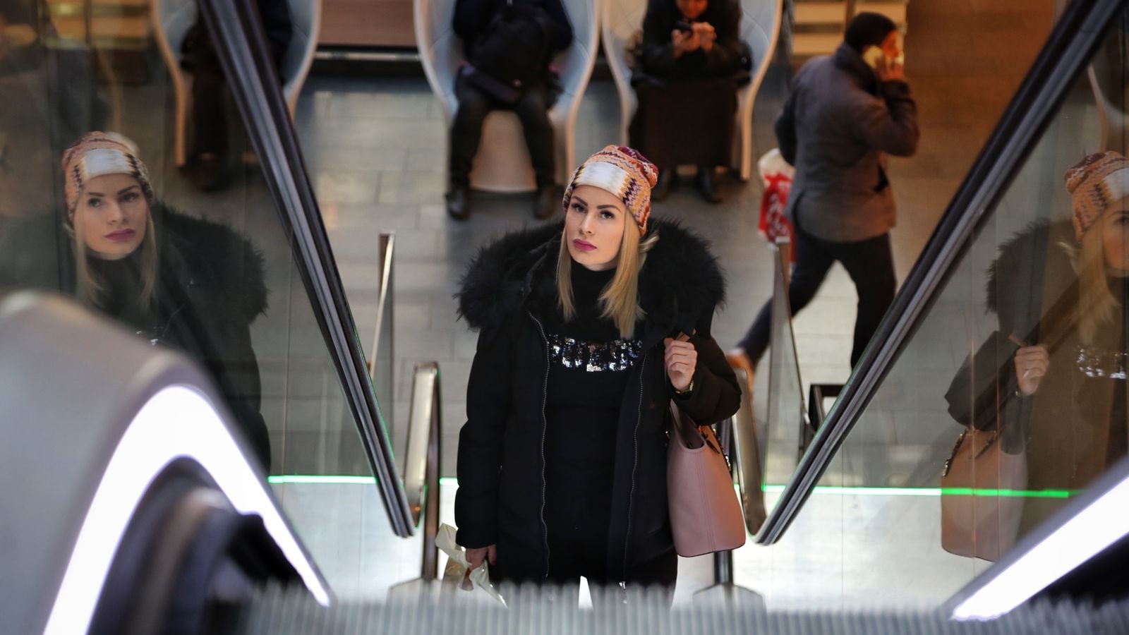 En ung kvinne kommer opp en rulletrapp på et kjøpesenter. Hun har vinterkær på seg og ser litt betenkt ut.