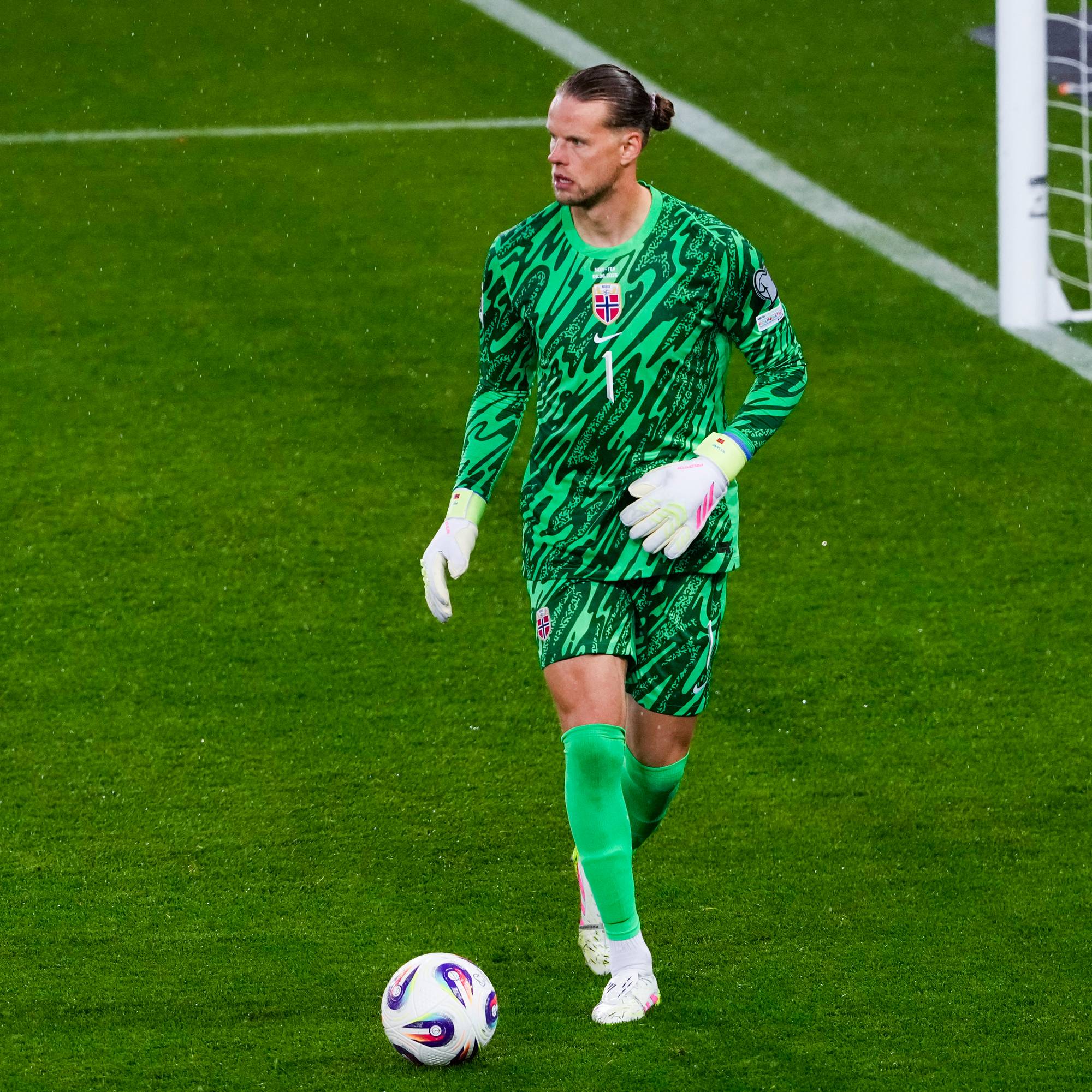 Keeperen i Norges grønne drakt står på en fotballbane. Han har på seg hansker og har ballen foran seg. (Bildebeskrivelsen er laget av en KI-tjeneste)