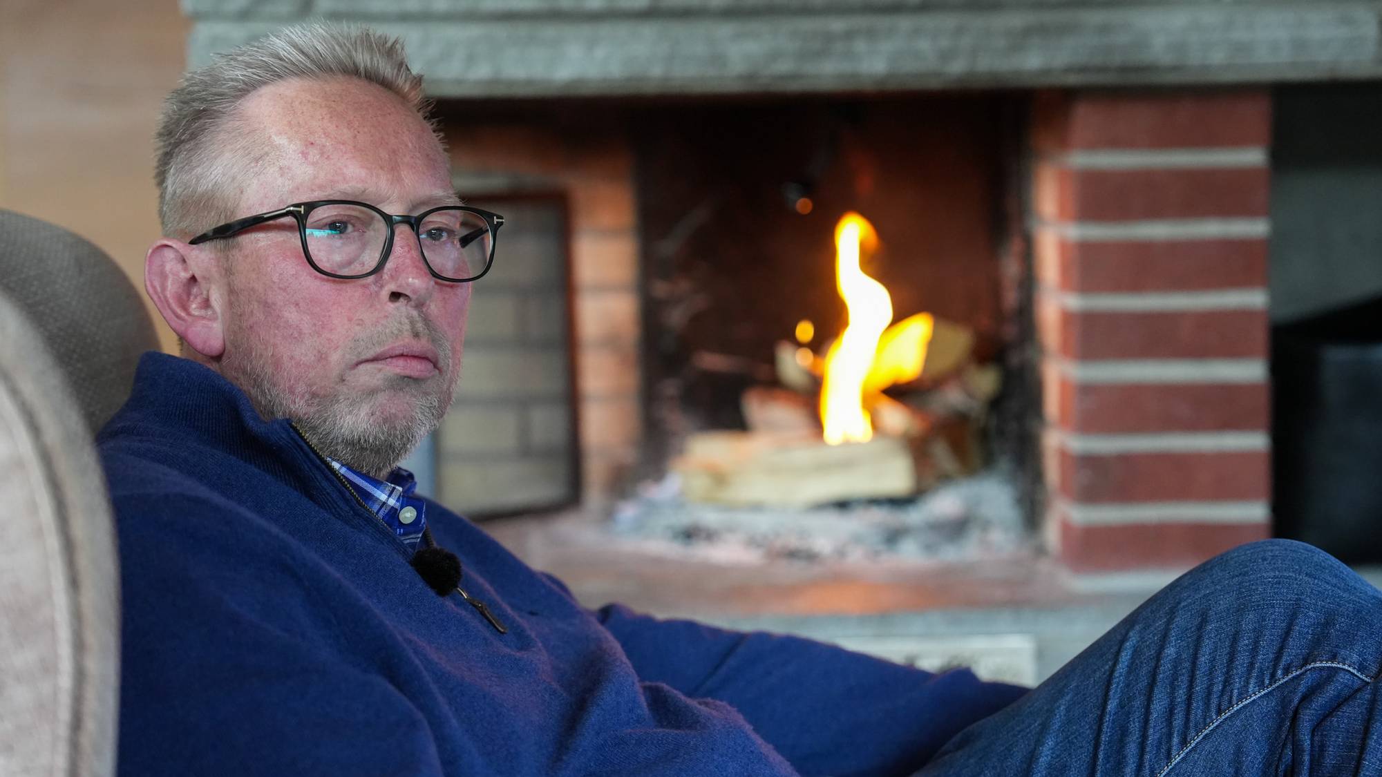 Man som sitter i godstolen foran peisen. 