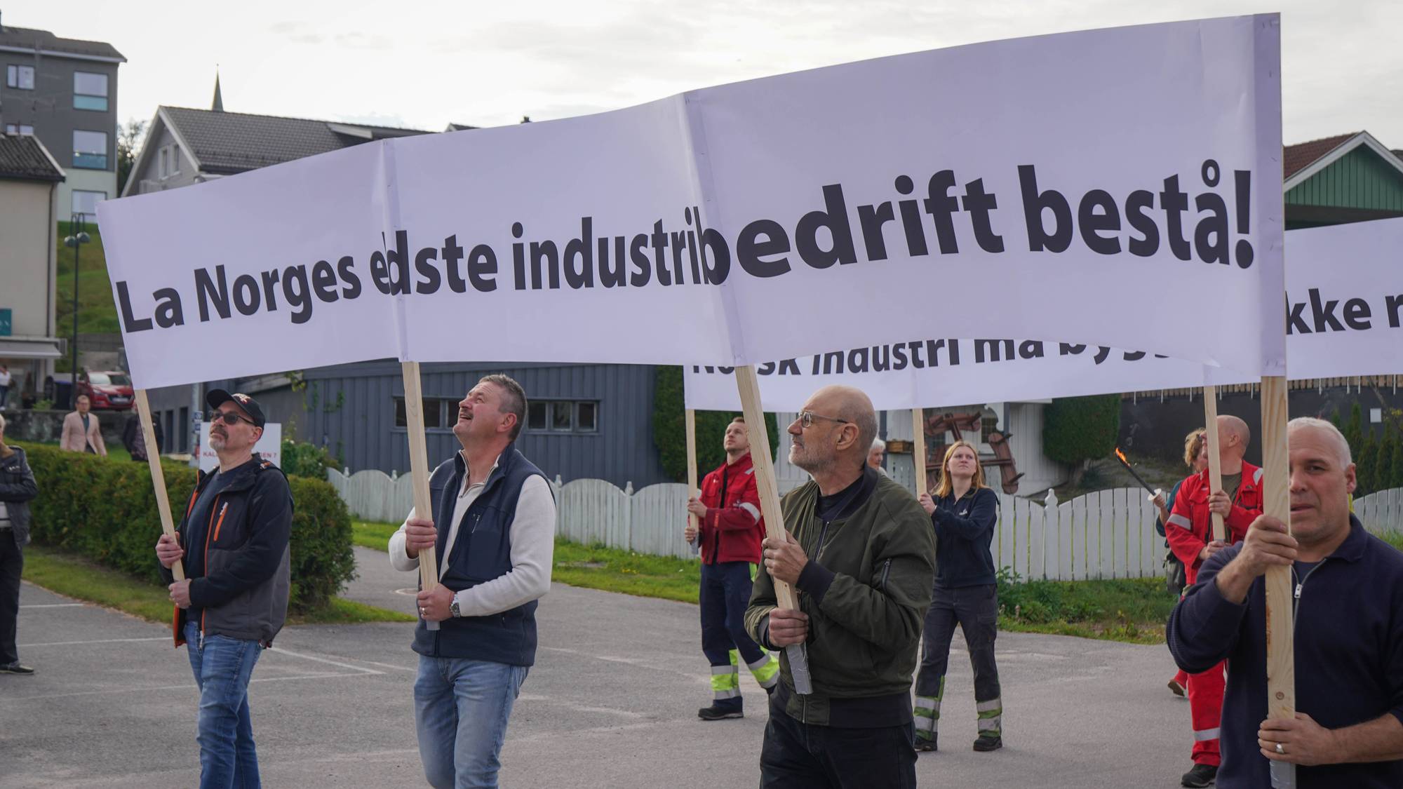 Demonstranter holder plakater med slagord for å bevare norsk industri i et utendørs opptog. (Bildebeskrivelsen er laget av en KI-tjeneste)