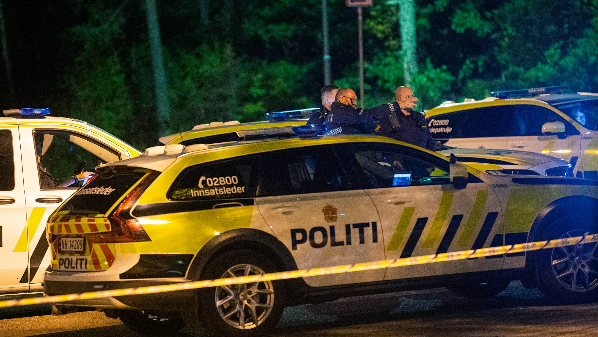 Flere politibiler står parkert ved et politi-sperrebånd i mørket. 