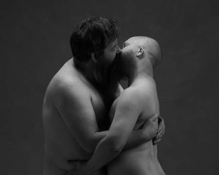 To menn med skjegg holder rundt hverandre og kysser.