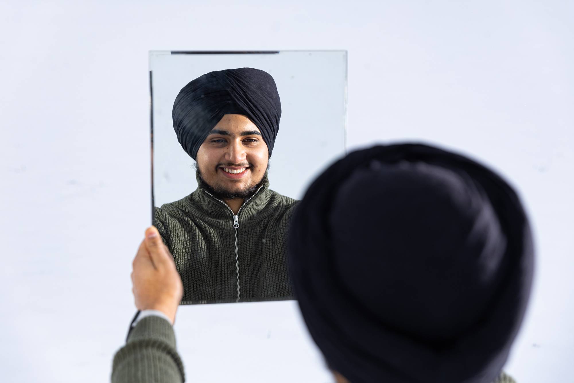 Vi ser over skulderen til Gurveer at det han holder i hendene er et speil, hvor han ser på seg selv med turban og smiler bredt. Han har også på seg en grønn genser. Det er snø og vinter rundt speilbildet.