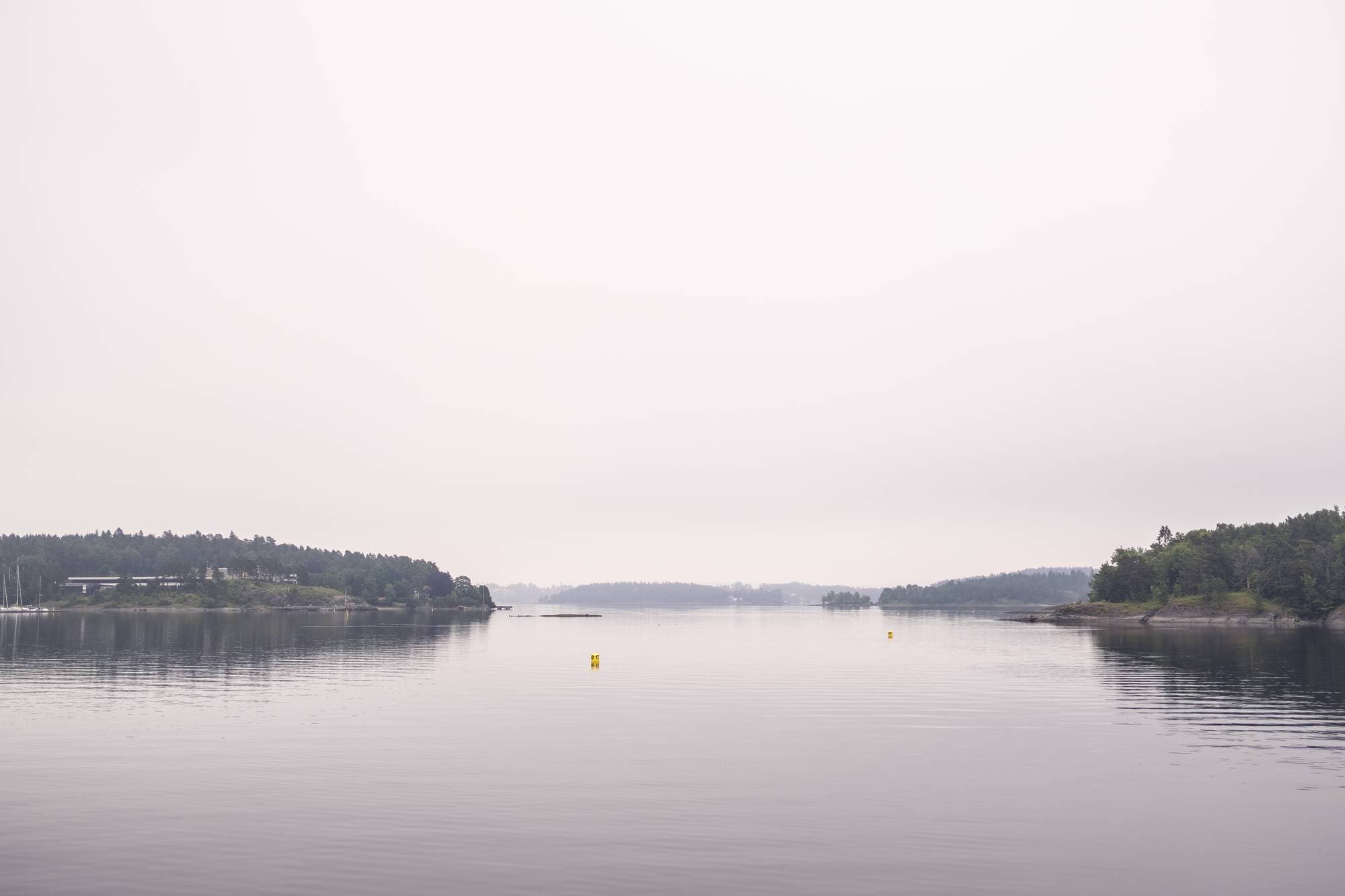 En vid fjord med tettbevokste øyer strekker seg innover i bildet. En bygning med lang fasade og flere vinduer ligger på en av øyene. Vanligvis er det mange fritidsbåter her. (Bildebeskrivelsen er laget av en KI-tjeneste)