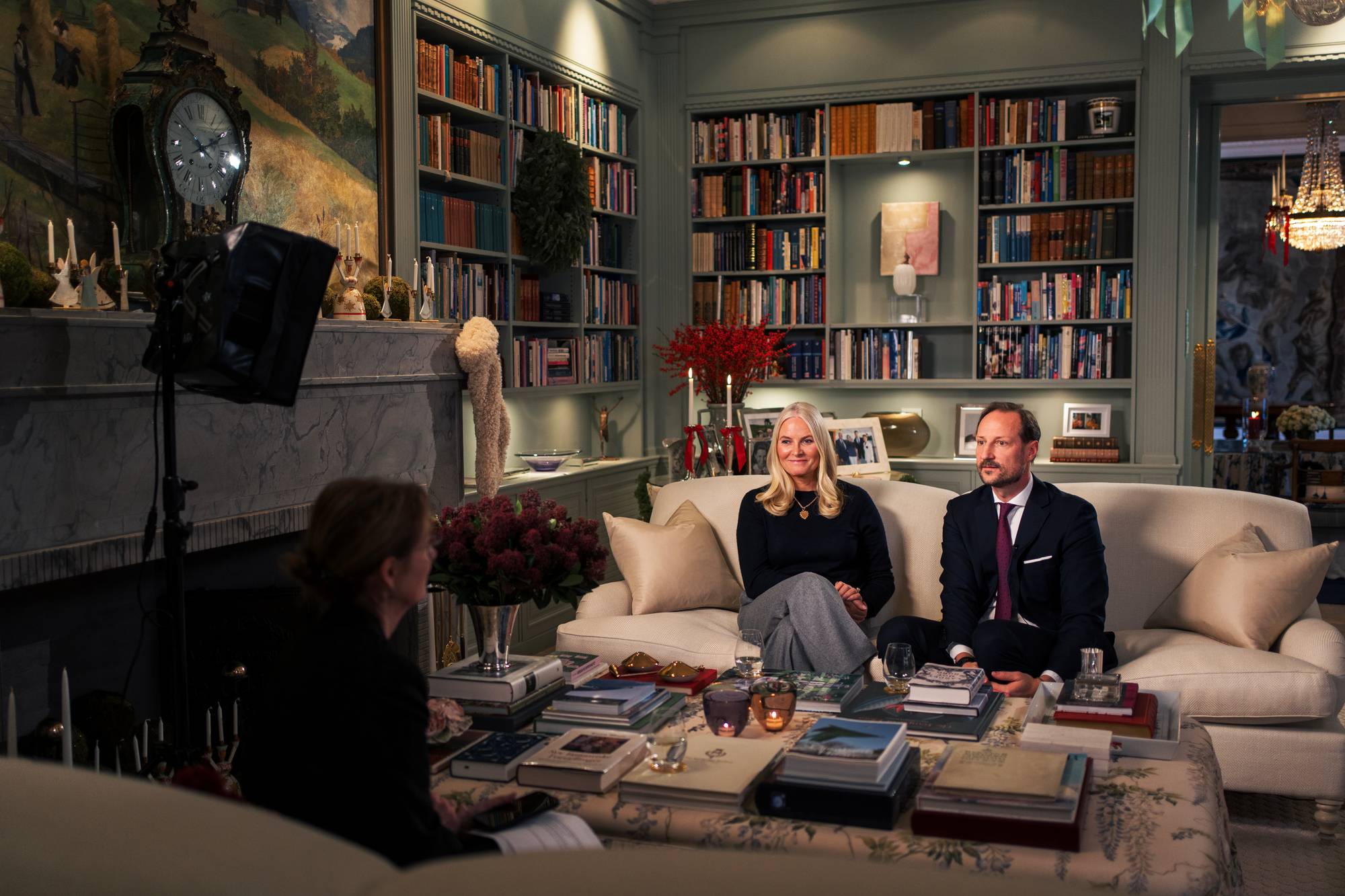 Kronprinsparet sitter i en lys sofa hjemme på Skaugum og blir intervjuet av NRK til "Året med kongefamilien 2025"