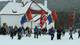 Eilif Aslaksen En gruppe mennesker med flagg, inkludert samiske flagg og det norske flagget, går i snøen. Bak dem er en hvit kirke med rødt tak. Det er trær i bakgrunnen. (Bildebeskrivelsen er laget av en KI-tjeneste)