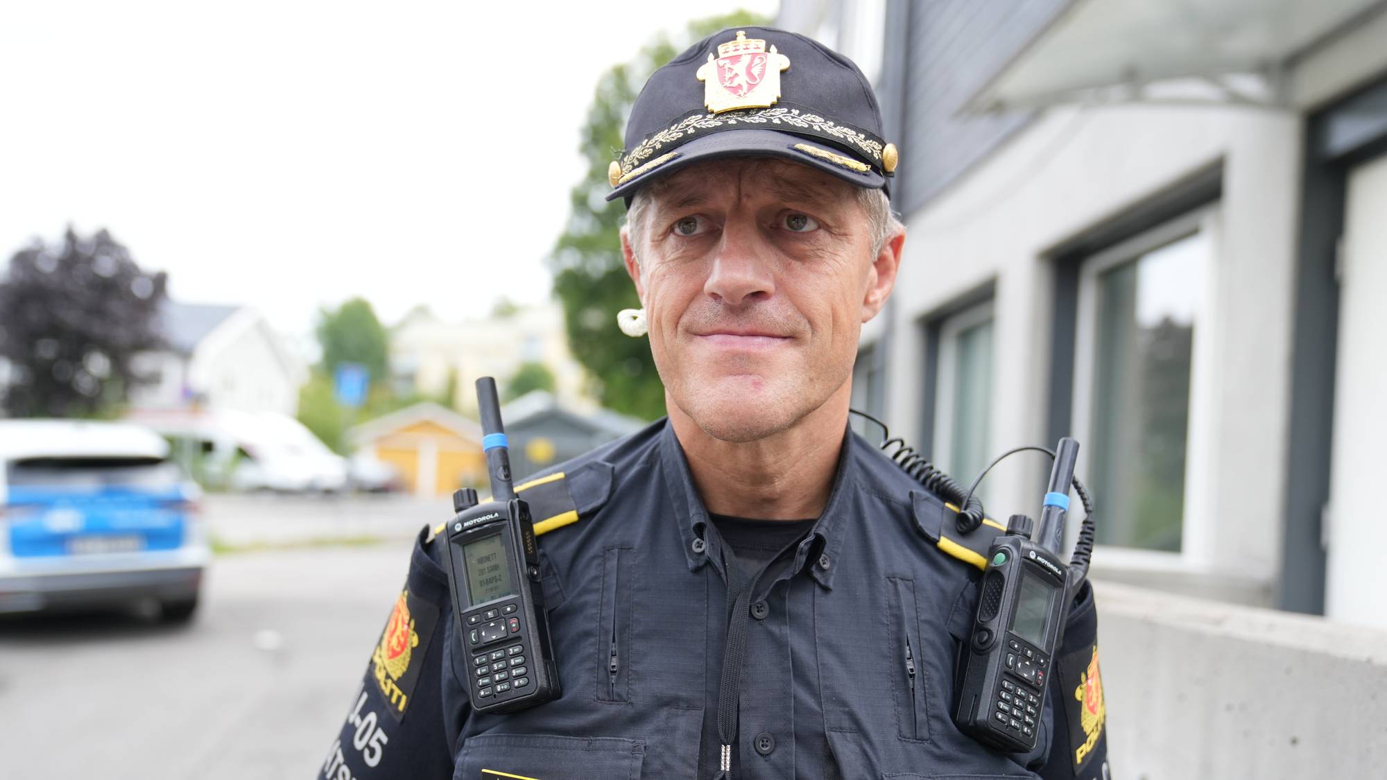 Politioverbetjent i uniform står utendørs med sambandsutstyr. (Bildebeskrivelsen er laget av en KI-tjeneste)