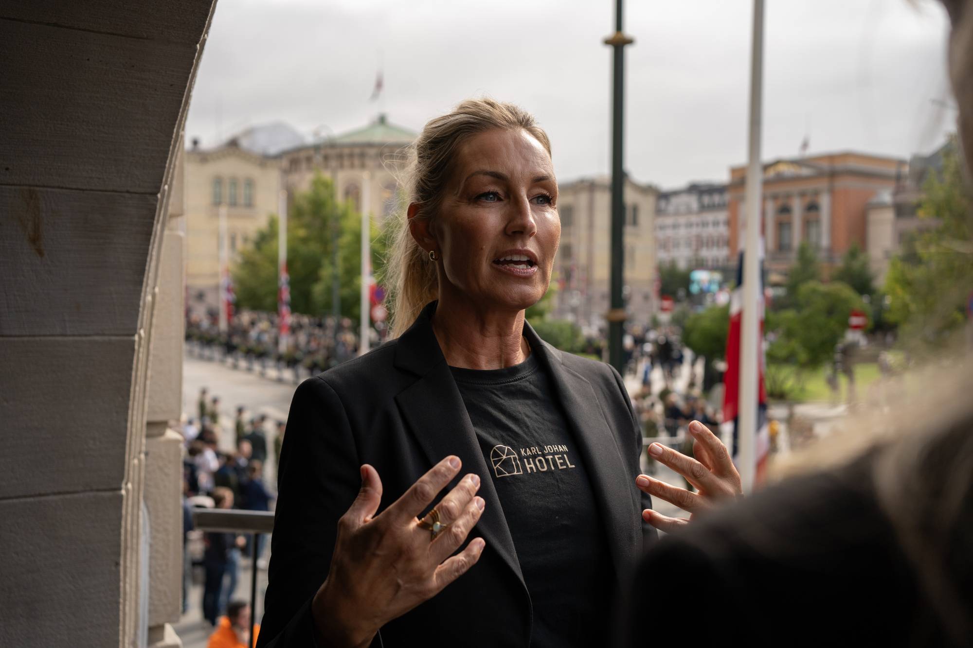 Kvinne i svart drakt snakker foran Stortinget i Oslo. (Bildebeskrivelsen er laget av en KI-tjeneste)