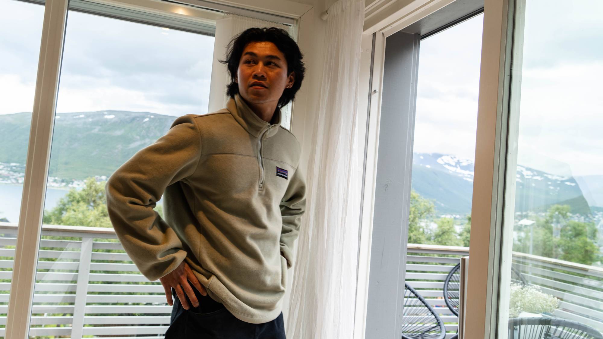 Mann i lys genser står innendørs foran store vinduer med utsikt til fjell. (Bildebeskrivelsen er laget av en KI-tjeneste)