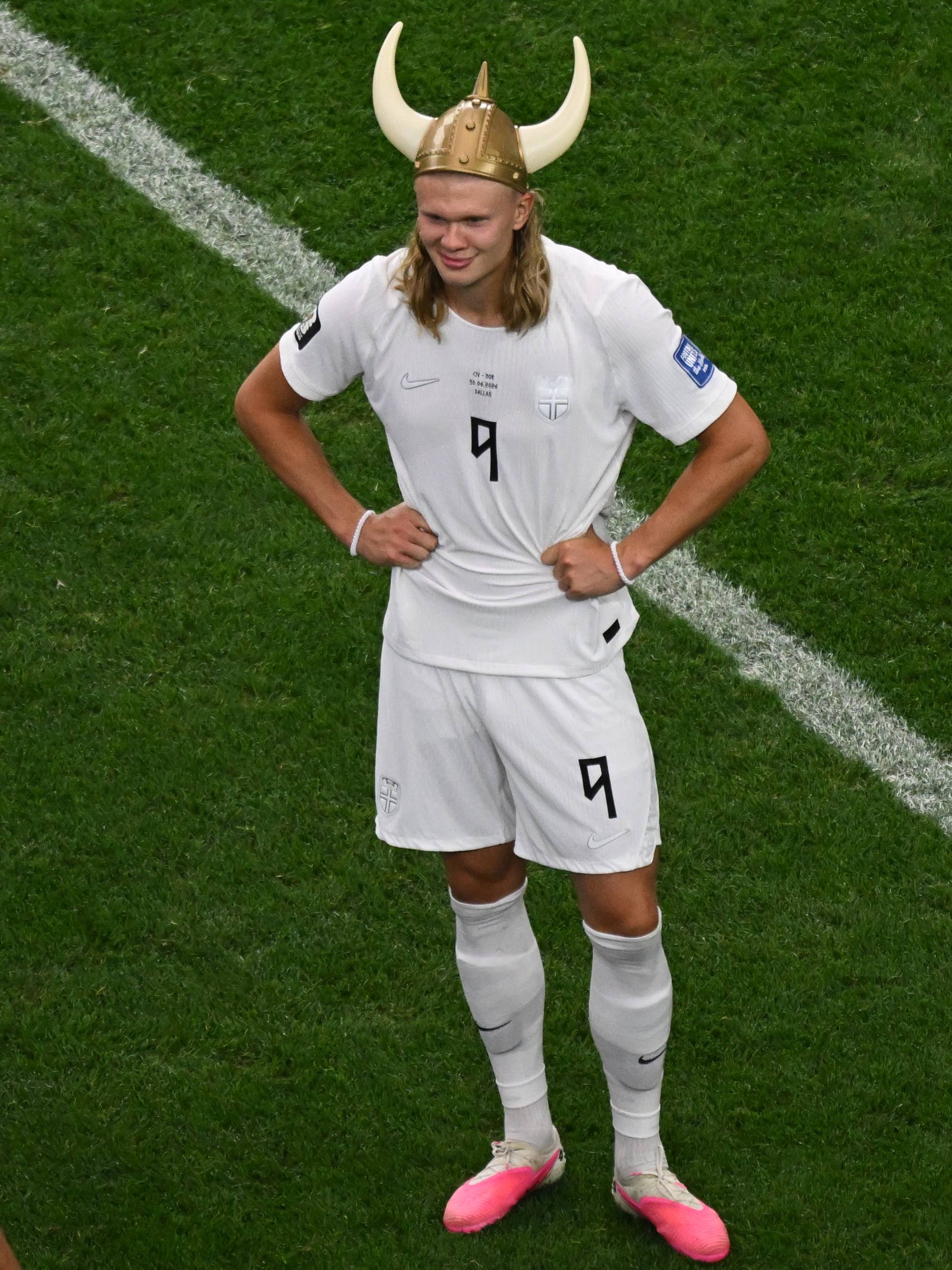 Erling Braut Haaland med vikinghjelm blir filmet av fotografer på en fotballbane. (Bildebeskrivelsen er laget av en KI-tjeneste)