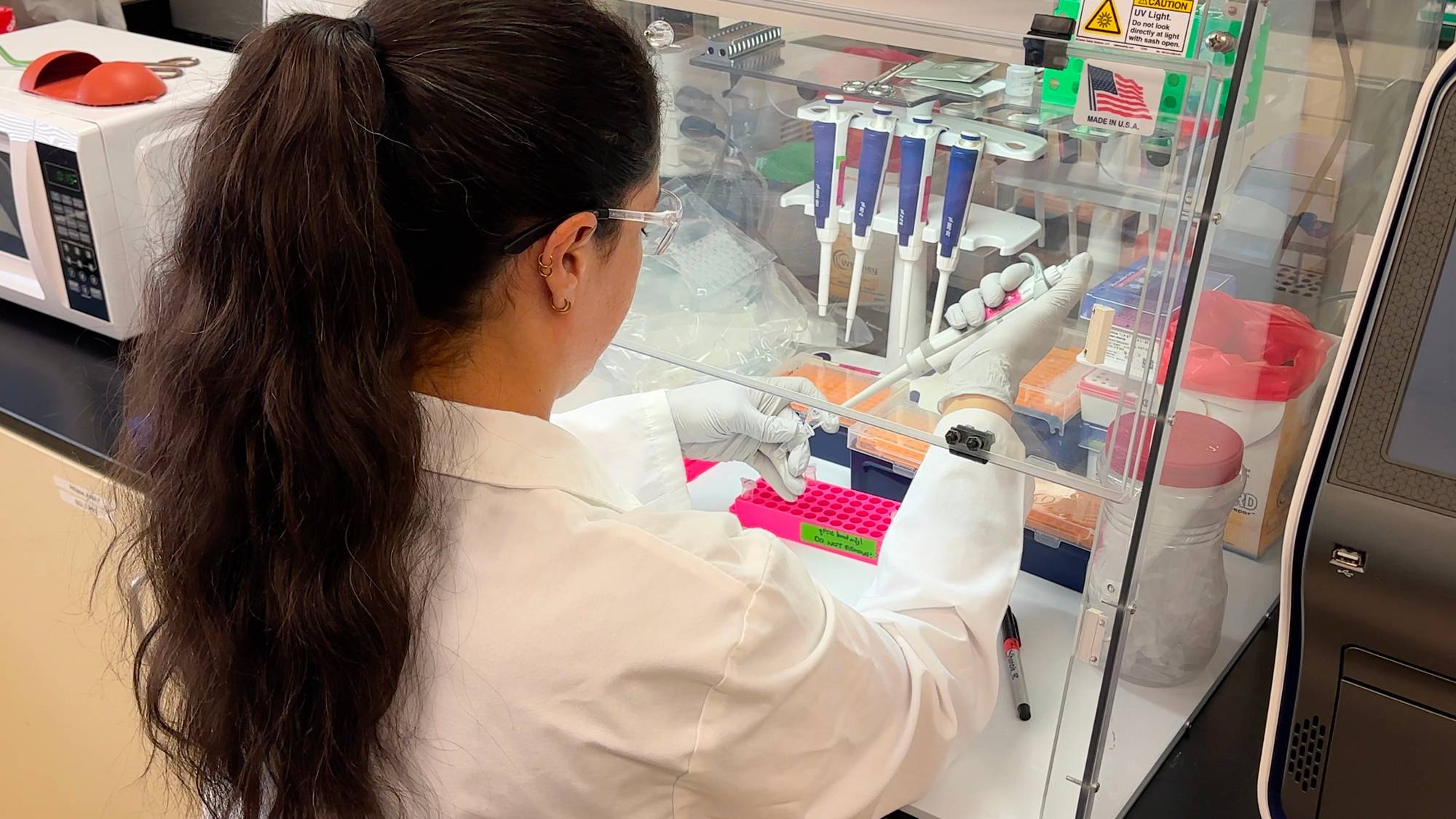 Forskning på hantavirus - En kvinne i hvit frakk og langt mørkt hår sitter i et laboratorium med sprøyter og reagensrør.