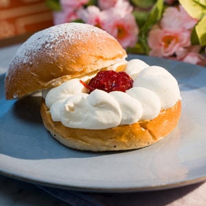 En fastelavnsbolle med syltetøy ligger med øverste del på skrå ved siden av underdelen slik at kremen og syltetøyet i midten er synlig.