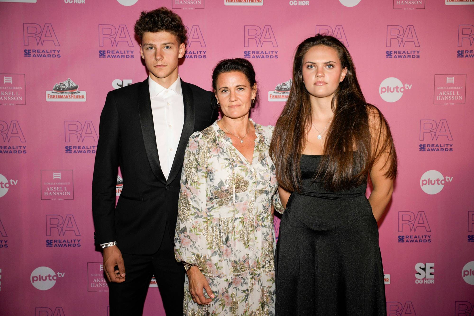 Kvinne med to ungdommer foran en rosa pressevegg under Reality Awards. (Bildebeskrivelsen er laget av en KI-tjeneste)