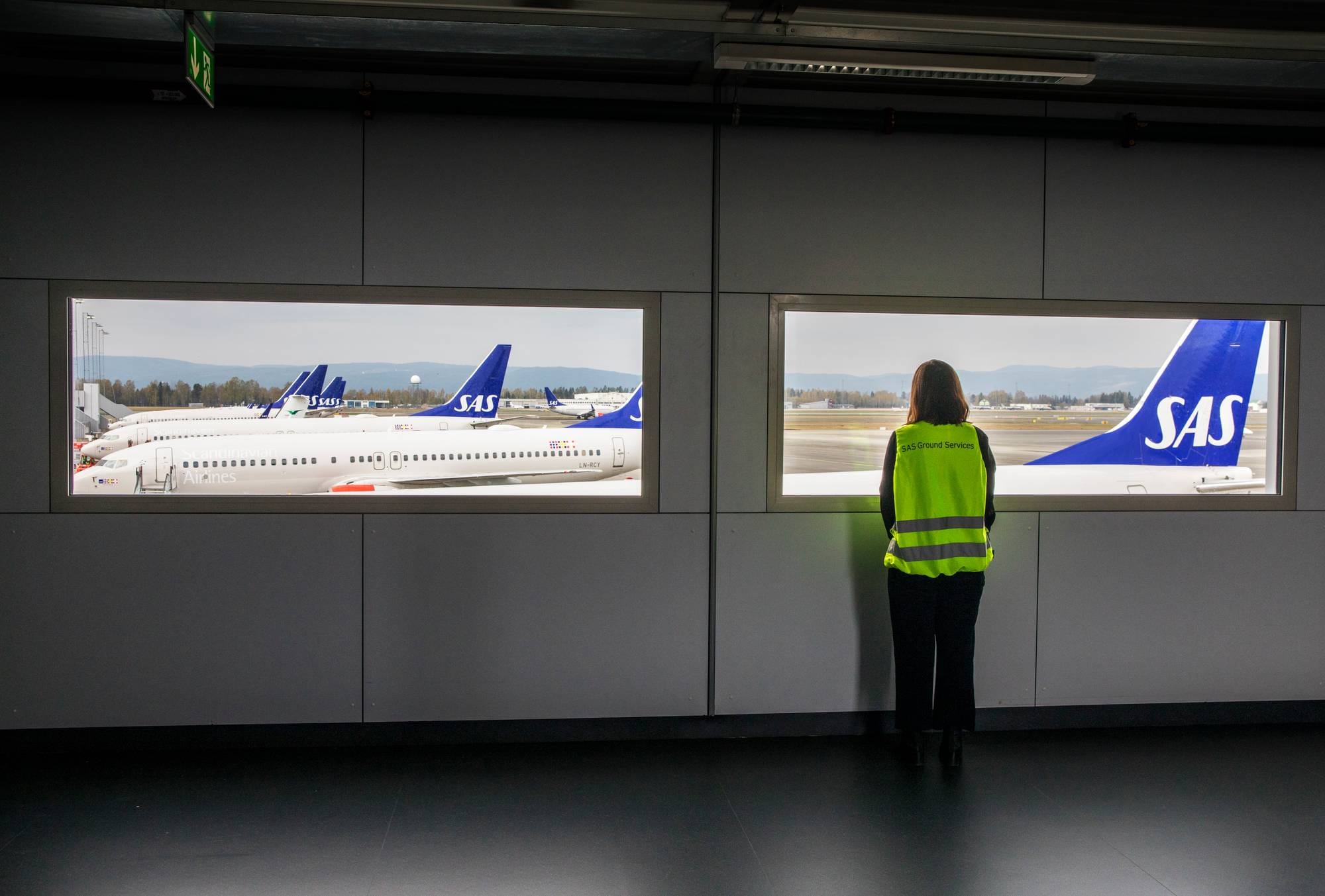 en person som står foran en et vindu og titter ut på en flyplass. 