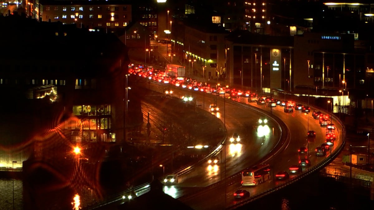 Kø av biler med røde baklys på en svingete vei om natten. Omgivelsene er opplyst av gatebelysning og bygninger. Glatte veier reflekterer lyset fra bilene. Det er tydelig tett trafikk. FOTO: NRK
