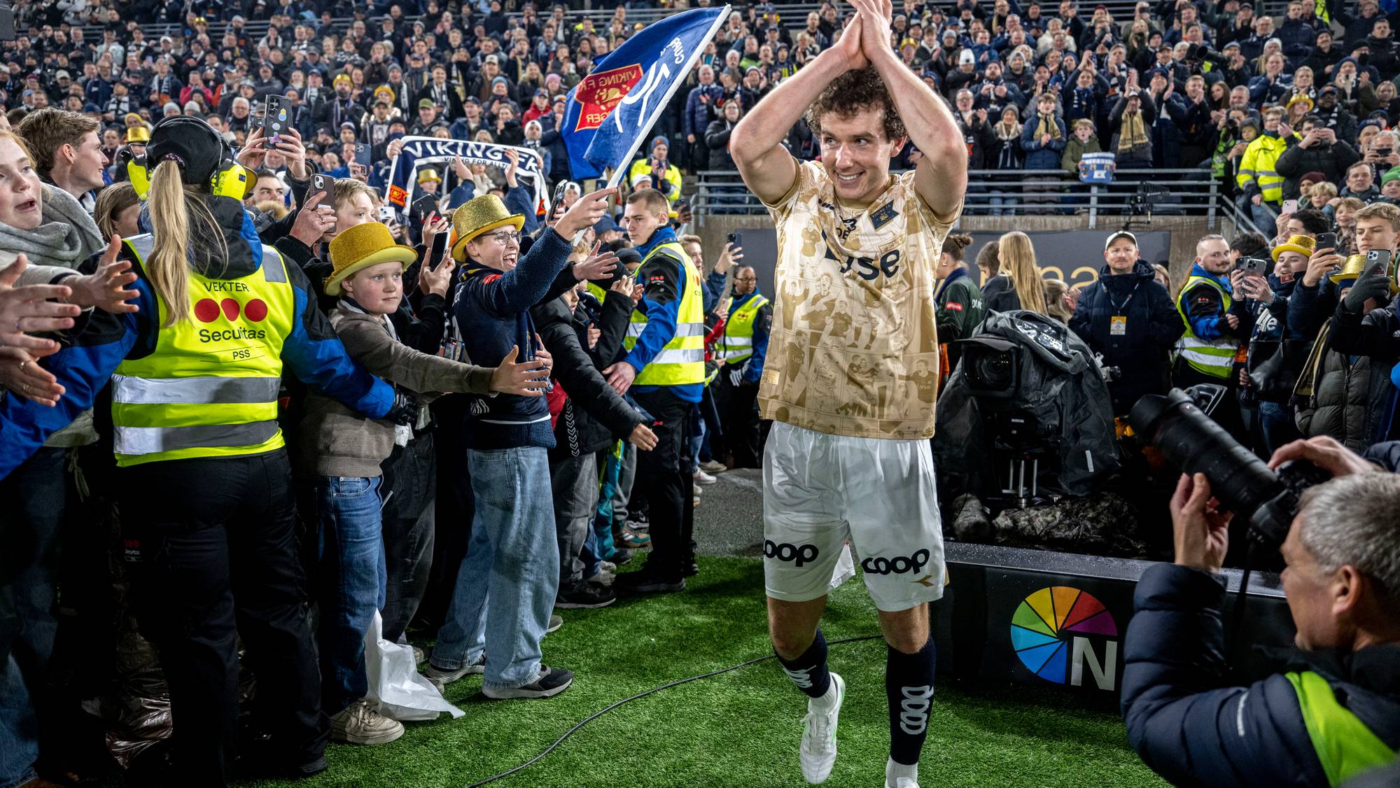 Fotballspiller takker publikum etter kamp. Tilskuere strekker seg mot ham foran en fullsatt tribune. (Bildebeskrivelsen er laget av en KI-tjeneste)