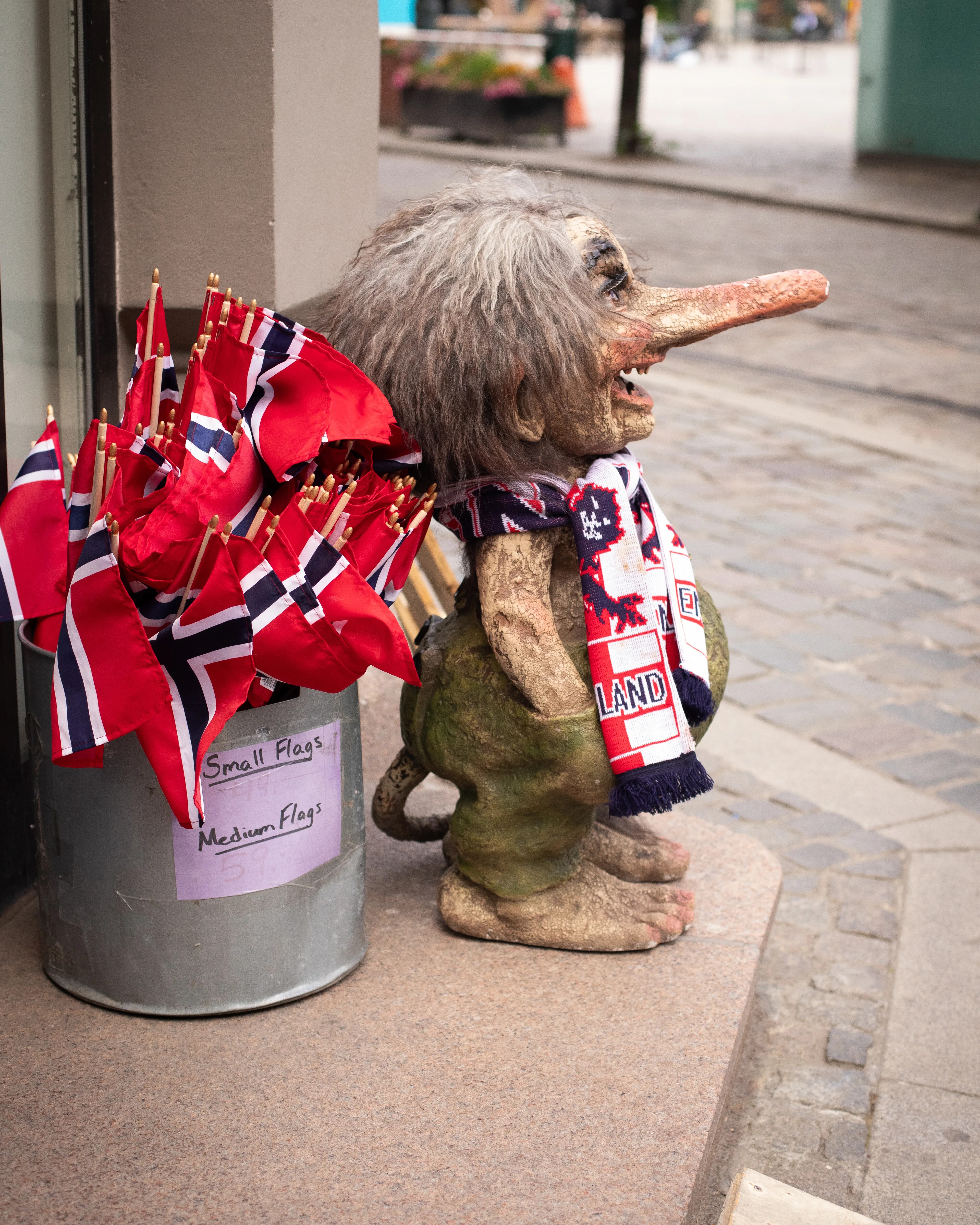 en troll figur med engelsk supporter skjerf, ved siden av står en bøtte med norske flagg