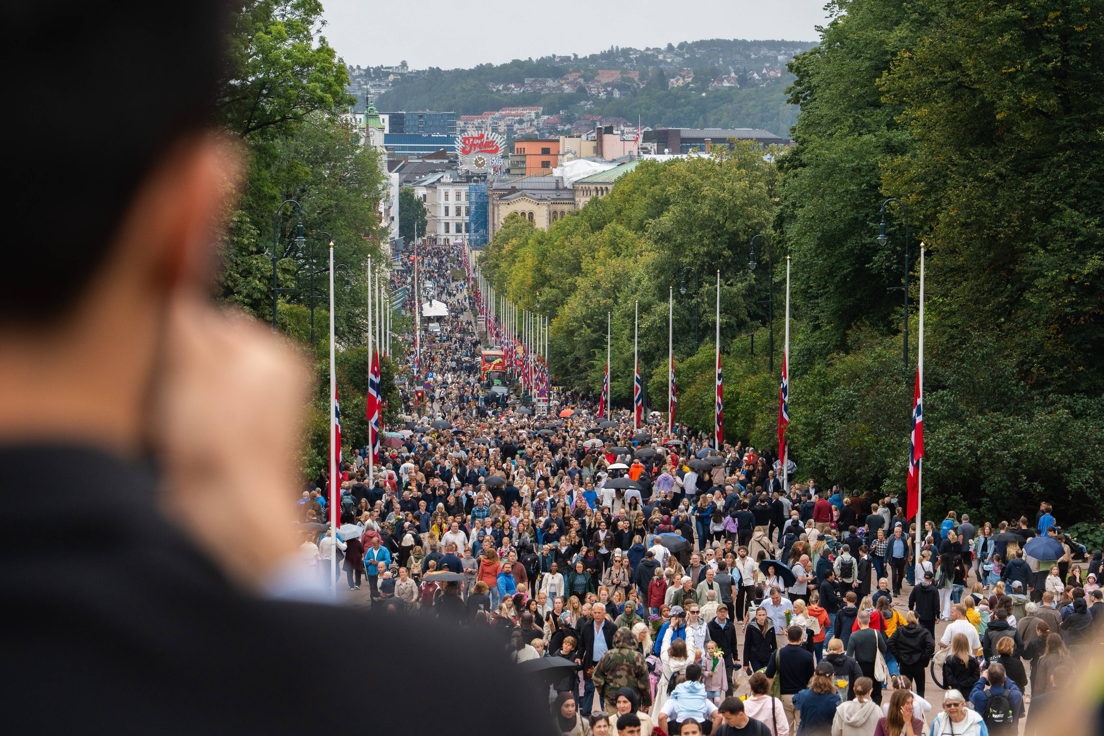 Fra slottsplassen lørdag 29 august 2026. Folkemasser på vei opp Karl Johans gate. Mann tar bilde med mobil.