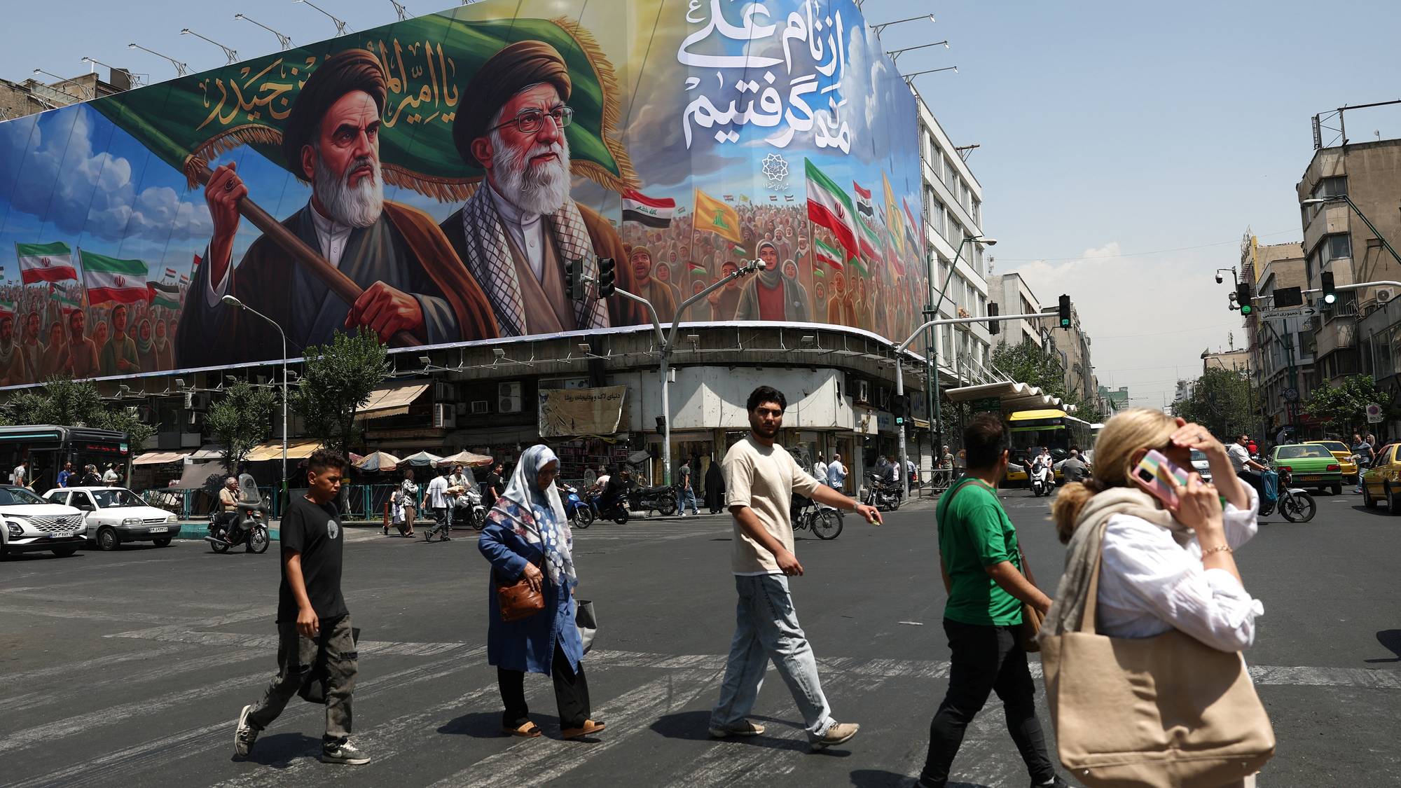Folk går fordi en enorm plakat av Irans øverste ledere. 