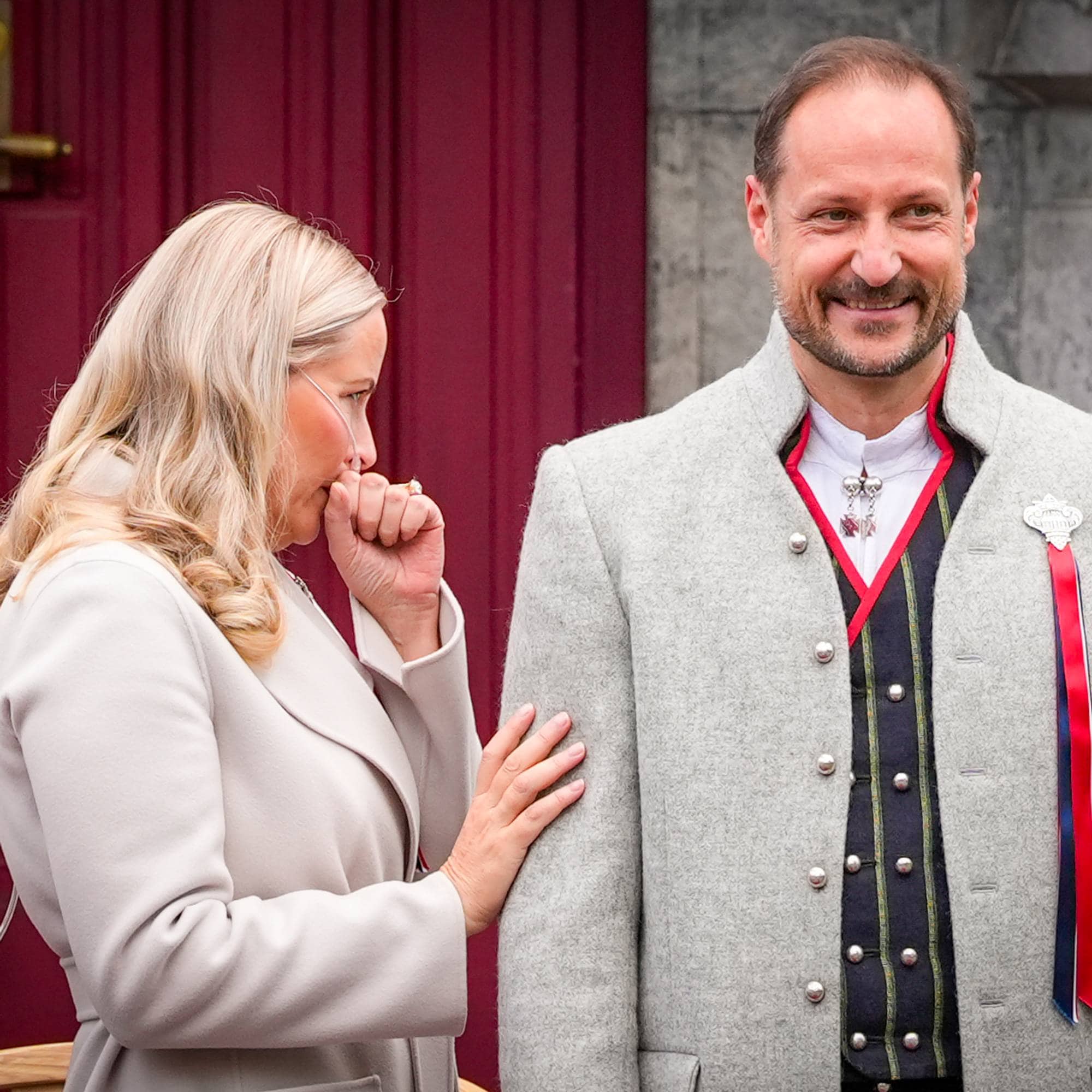 Kronprinsesse Mette-Marit snur seg mens hun hoster, ved siden av henne på trappen på Skaugum på 17. mai 2026 står kronprins Haakon