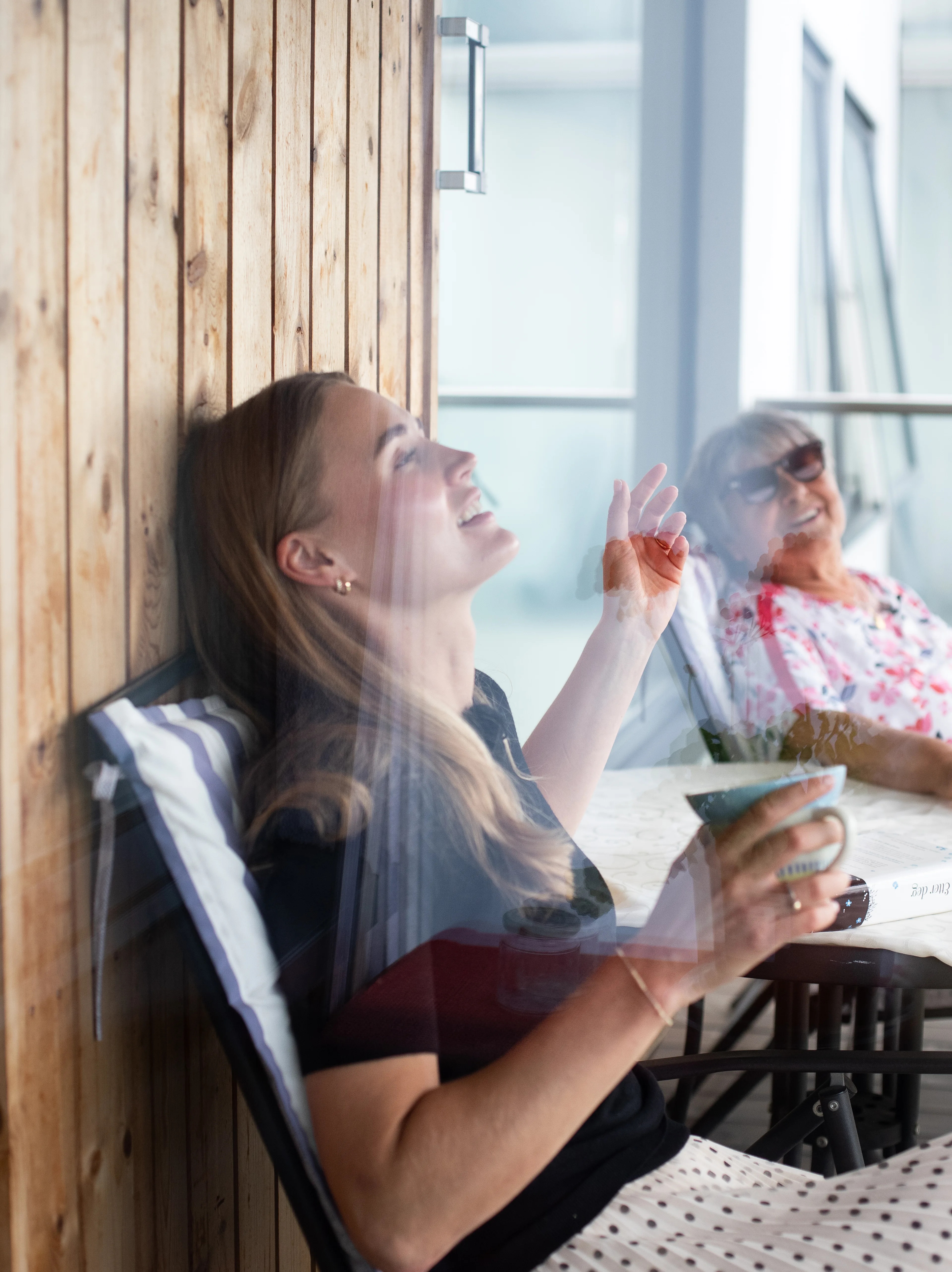 en eldre kvinne og en ung kvinne som sitter i stoler ved et bord på en balkong