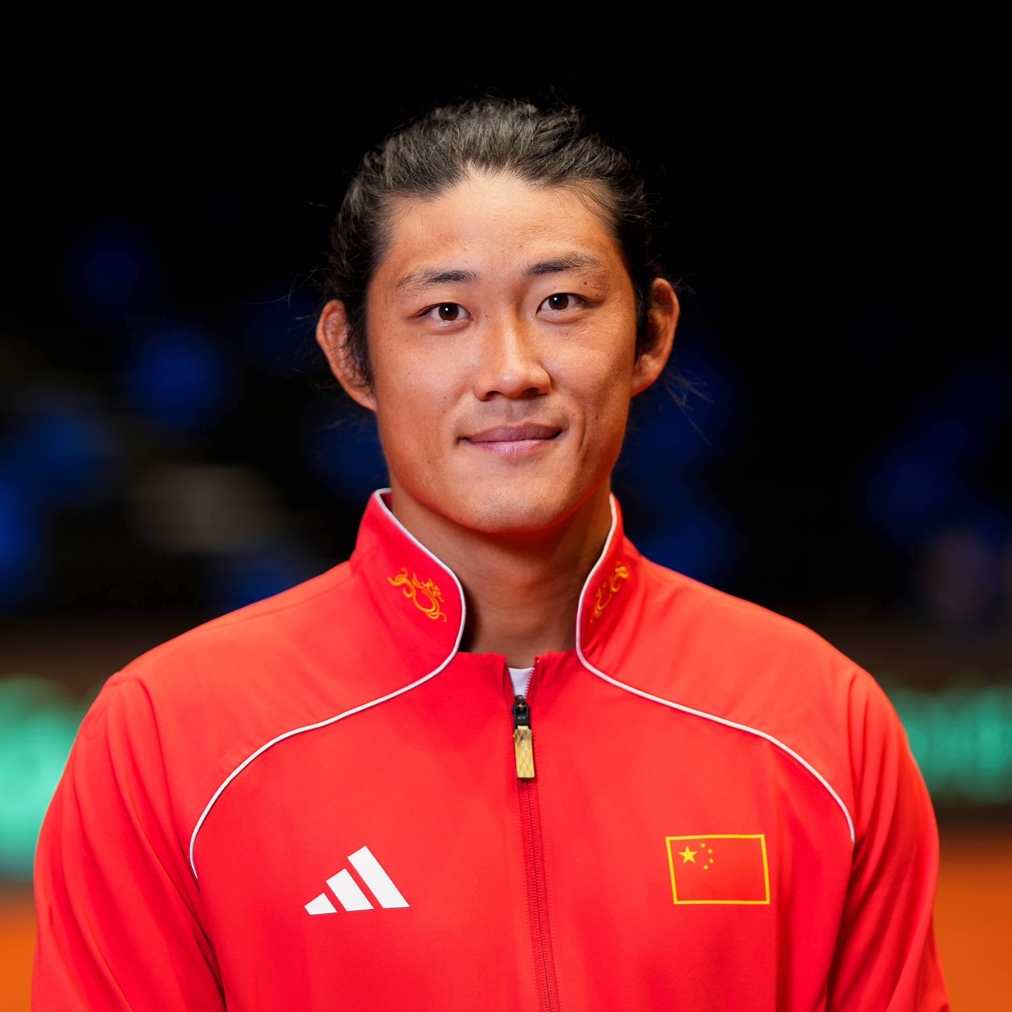 Portrett av en kinesisk utøver i rød treningsjakke på en tennisbane. (Bildebeskrivelsen er laget av en KI-tjeneste)