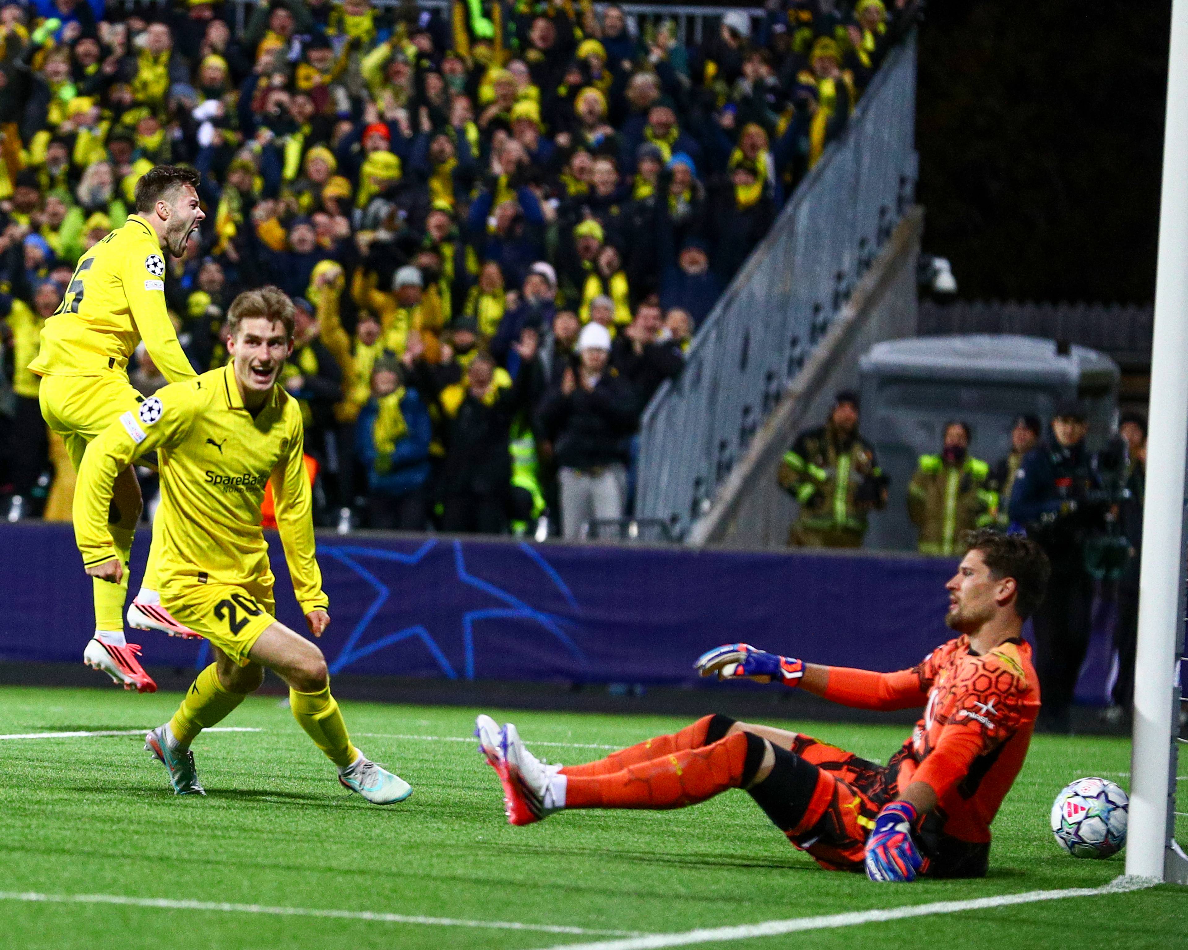 To fotballspillere i gult jubler etter scoring mot en sittende keeper i oransje drakt. (Bildebeskrivelsen er laget av en KI-tjeneste)