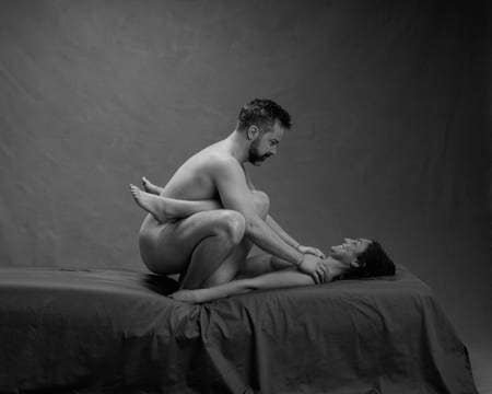 En naken mann sitter på huk med føttene til en naken kvinne rundt magen
