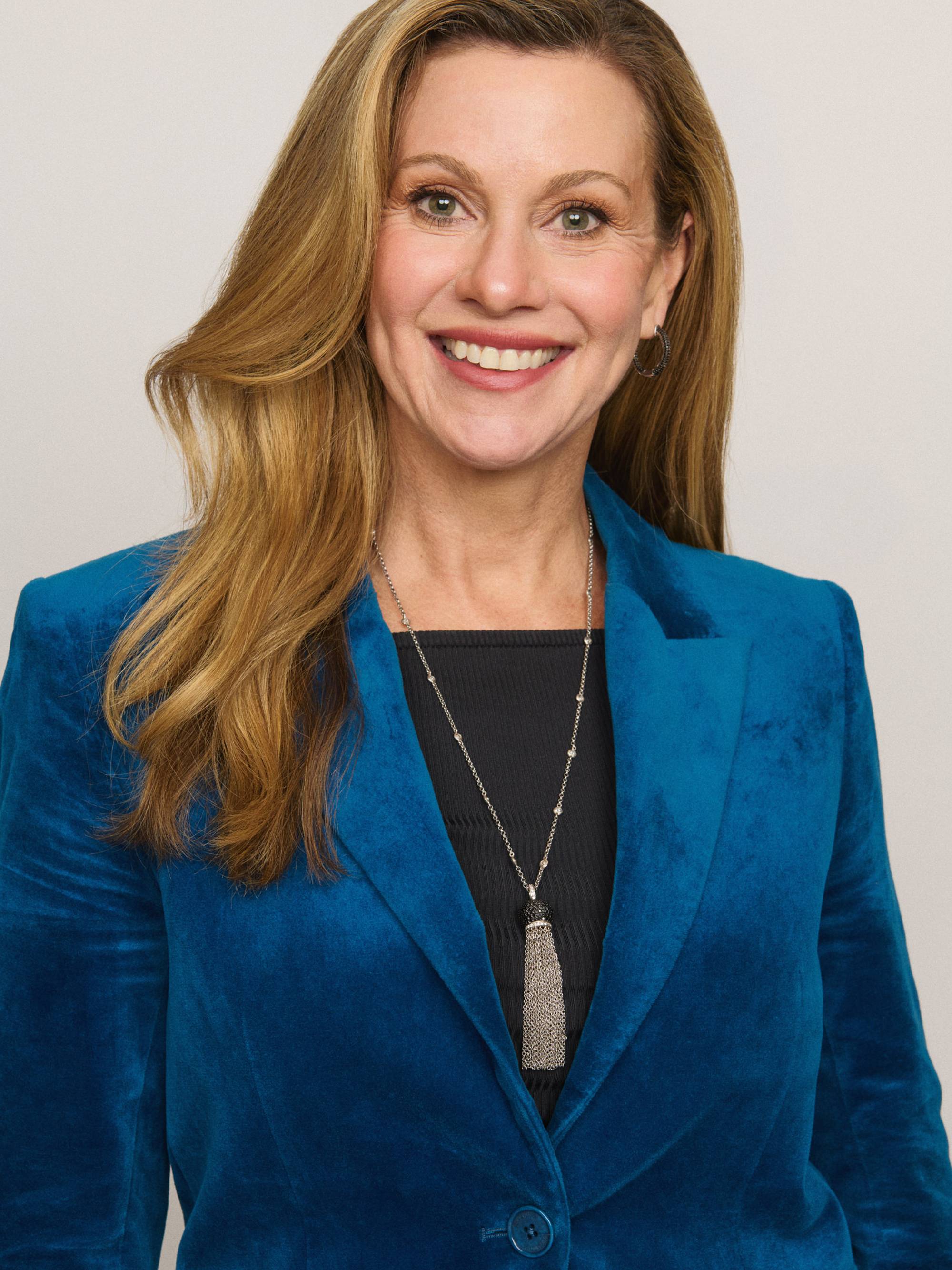 Bilde av Julie Inman Grant. Hun har på en blå dressjakke, kjede og sort topp. Det er et portrettbilde og hun smiler til kamera. Hun har langt blondt hår og lys hud. 
