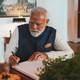 Stian Lysberg Solum / NTB Indias statsminister Narendra Modi sitter ved et skrivebord og skriver i en bok. Han er iført en hvit skjorte og en mørkeblå vest.