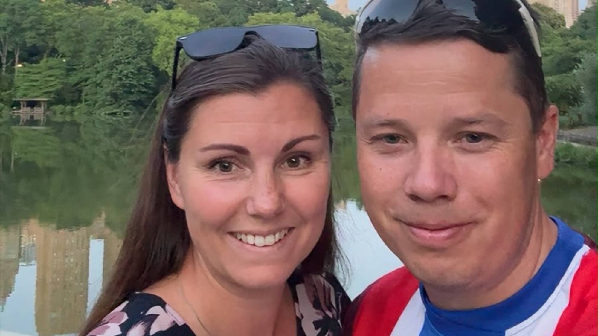 En kvinne og en mann tar en selfie foran en innsjø og bygårder i New York. (Bildebeskrivelsen er laget av en KI-tjeneste)