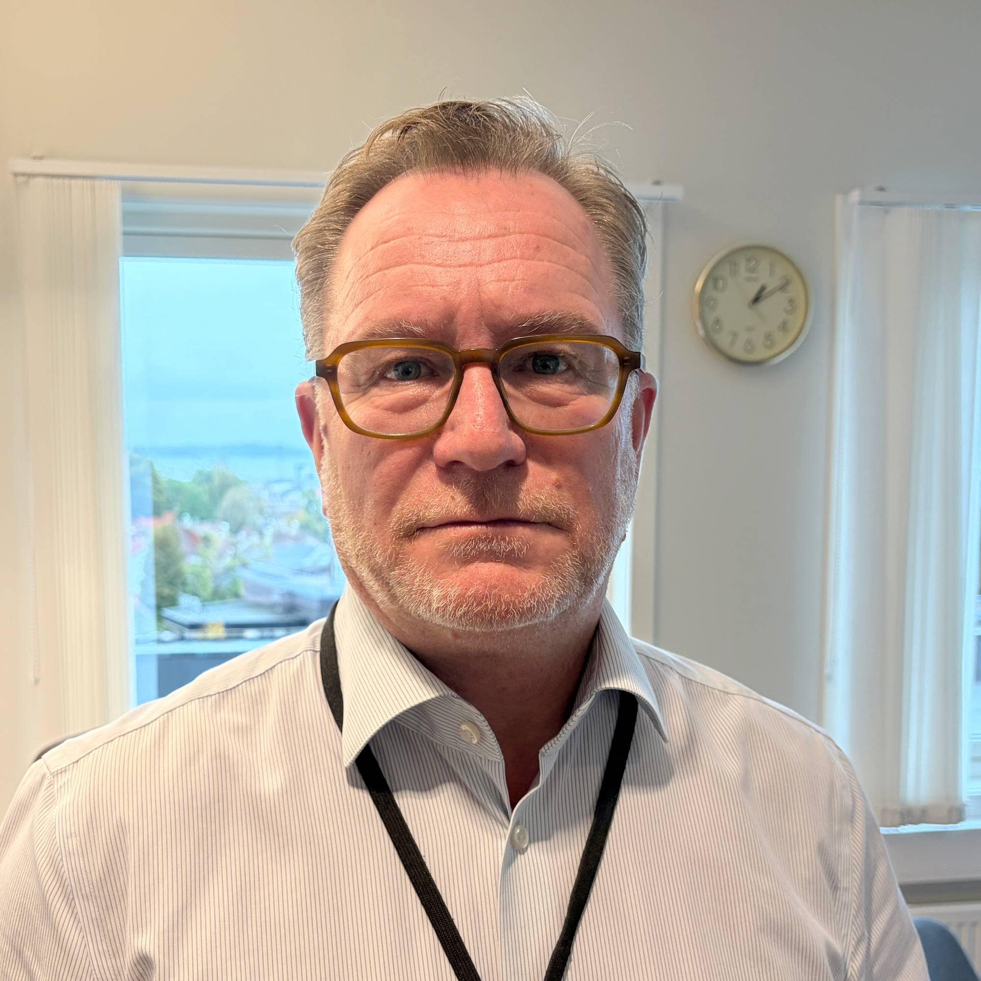 Man i lys skjorte med briller poserer på et kontor.