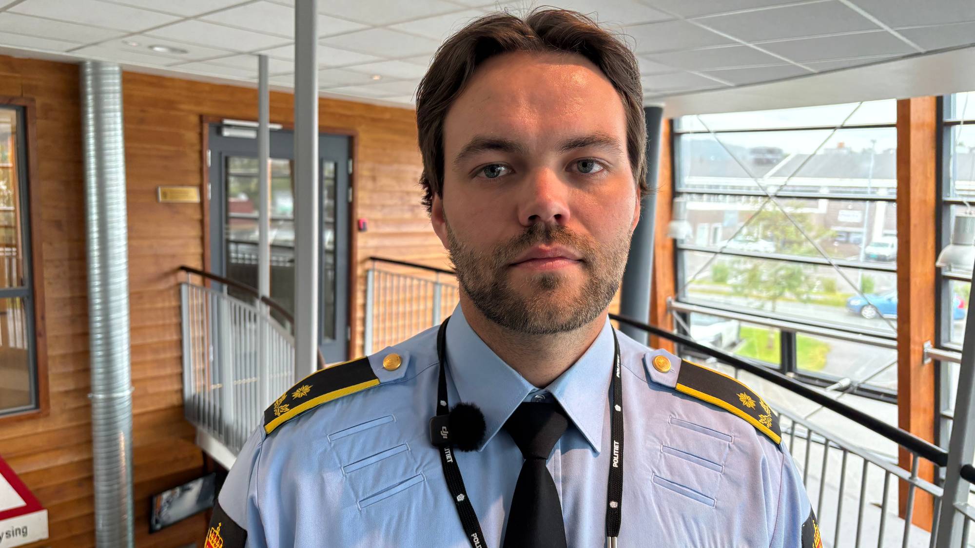 Mann i norsk politiuniform står inne i et lyst bygg. (Bildebeskrivelsen er laget av en KI-tjeneste)