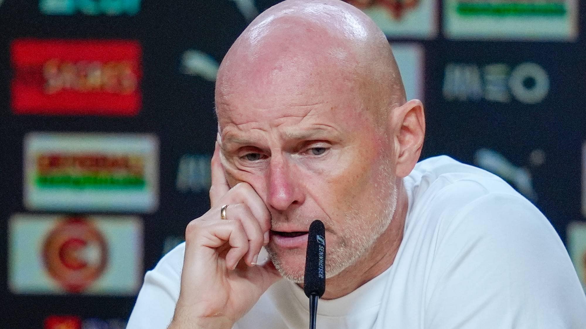 Ståle Solbakken under en pressekonferanse med sponsortavle i bakgrunnen. (Bildebeskrivelsen er laget av en KI-tjeneste)