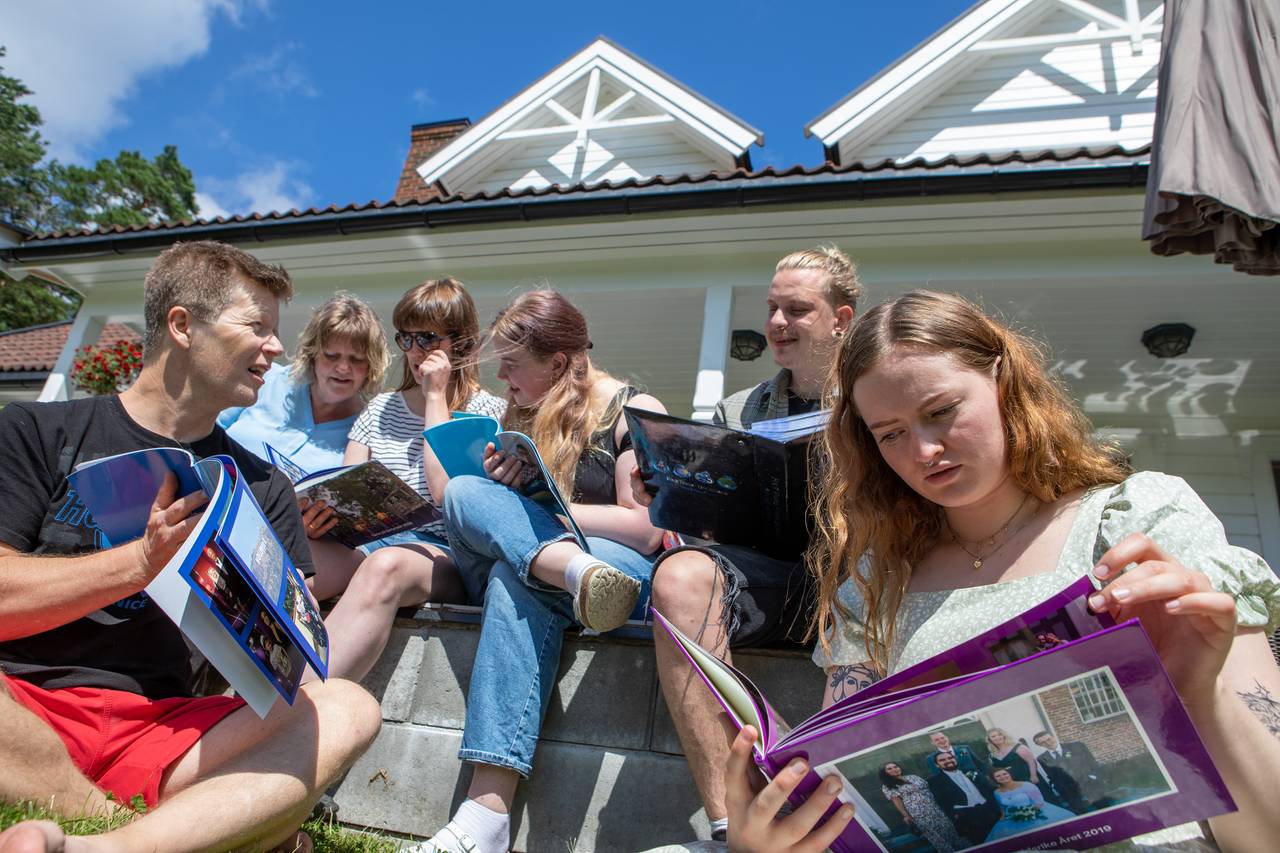 Seks familiemedlemmer sitter ute i sola og kikker i album.