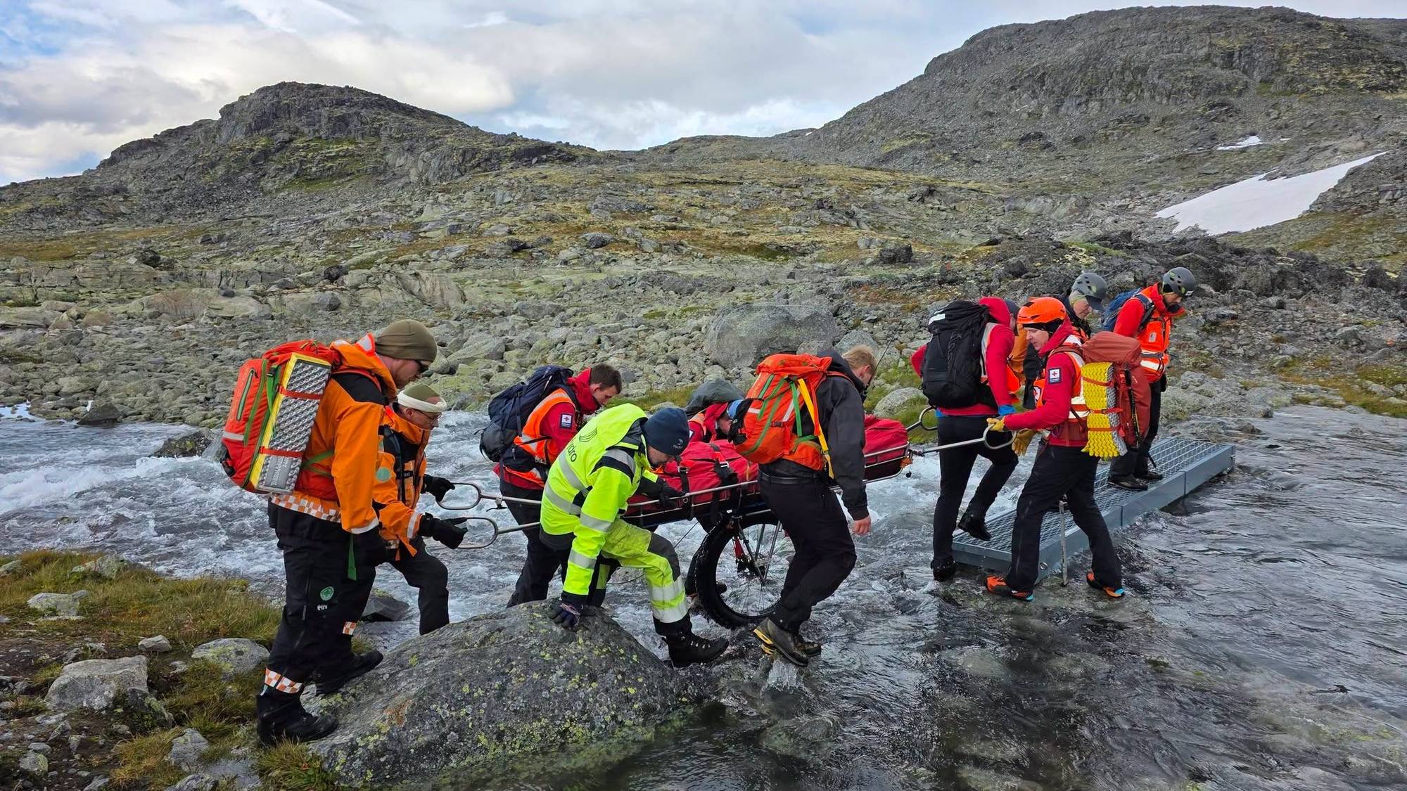 Redningsmannskap som berer båre over ein bekk.