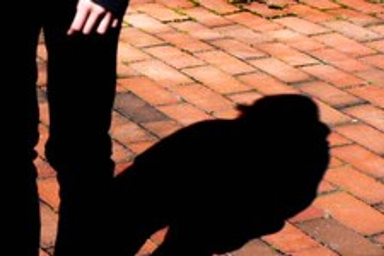 Bildet viser bena på en person og en hånd samt skyggen til personen på rød belegningsstein.