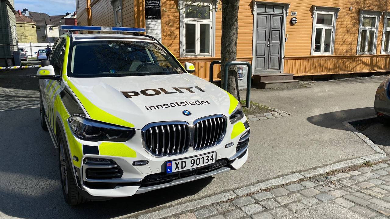 En politibil står parkert i gata hvor politiet nå etterforsker drap i Trondheim. I bakgrunnen ser vi en gul bygård.