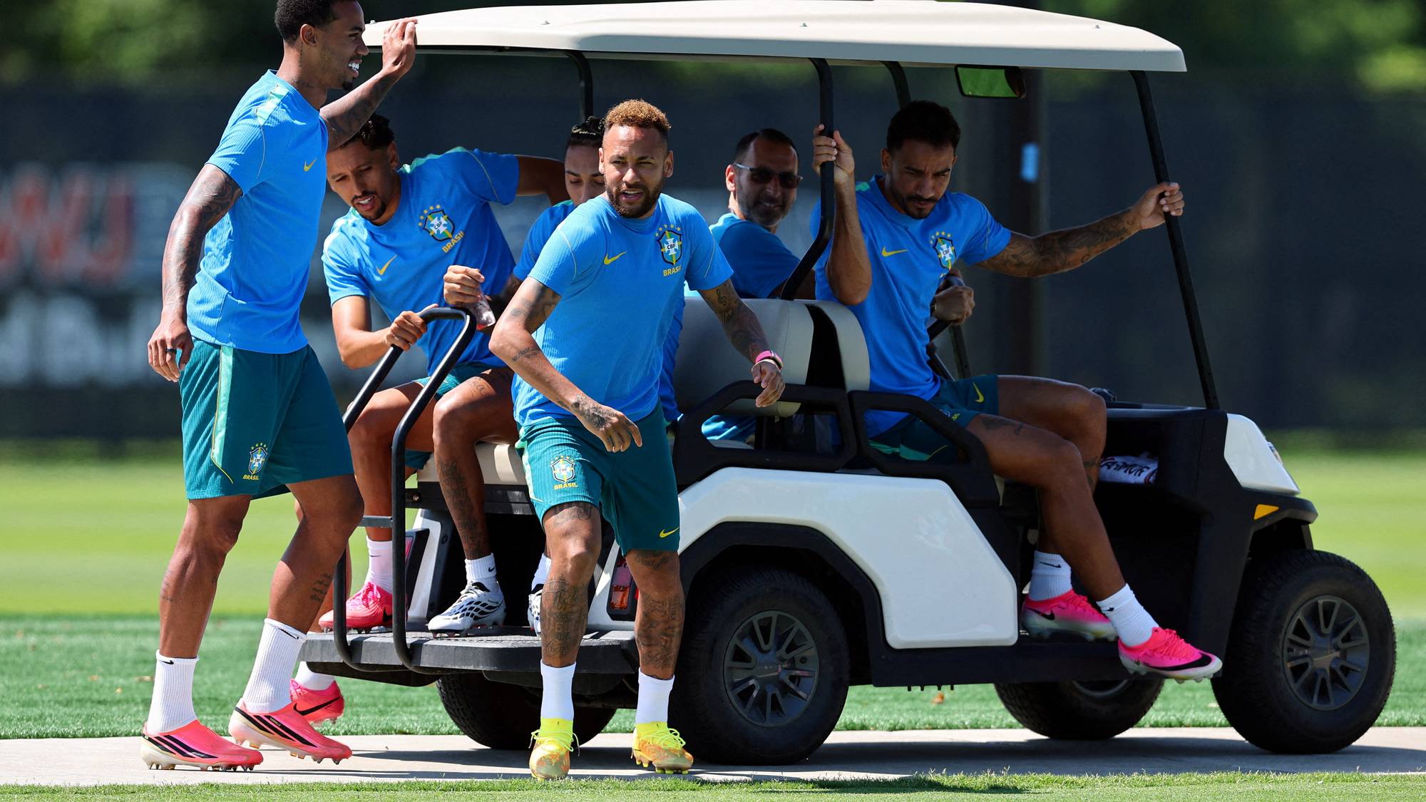 Brasilianske fotballspillere i treningsdrakter samlet rundt en golfbil på en gressbane. (Bildebeskrivelsen er laget av en KI-tjeneste)