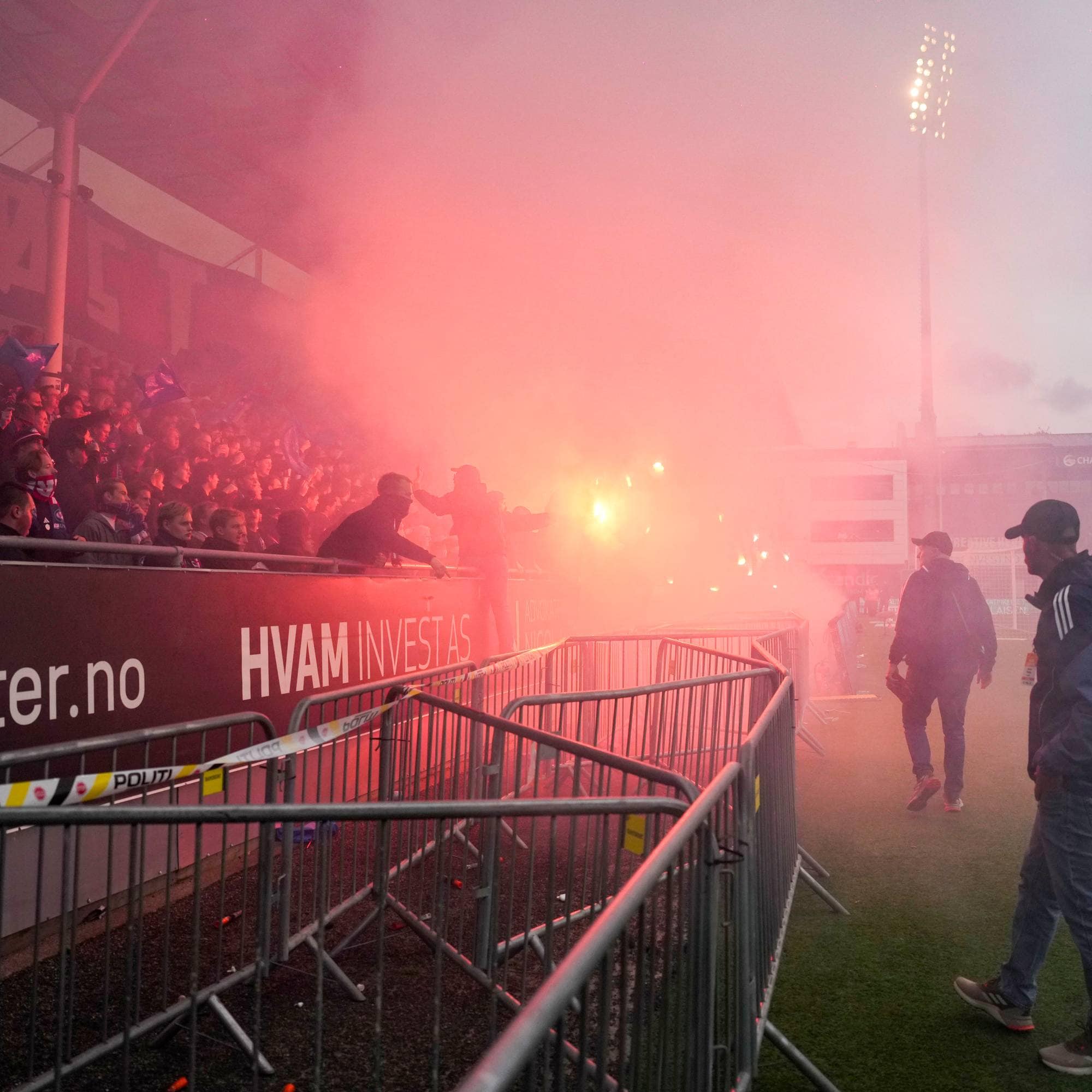 Supportere på en fotballtribune tenner røykbluss, som fyller deler av stadion med rød røyk. (Bildebeskrivelsen er laget av en KI-tjeneste)