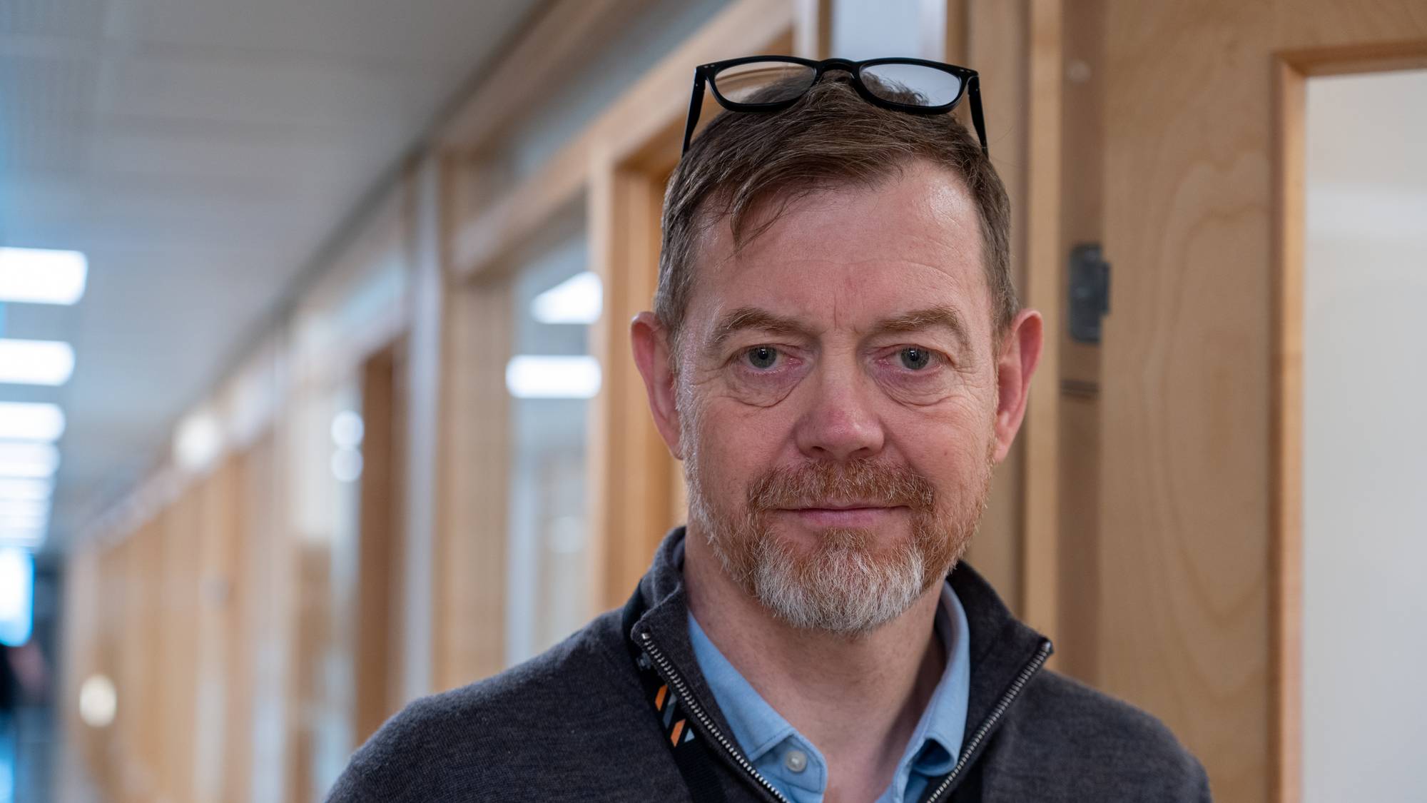 Mann med briller i pannen står i en kontorkorridor. (Bildebeskrivelsen er laget av en KI-tjeneste)