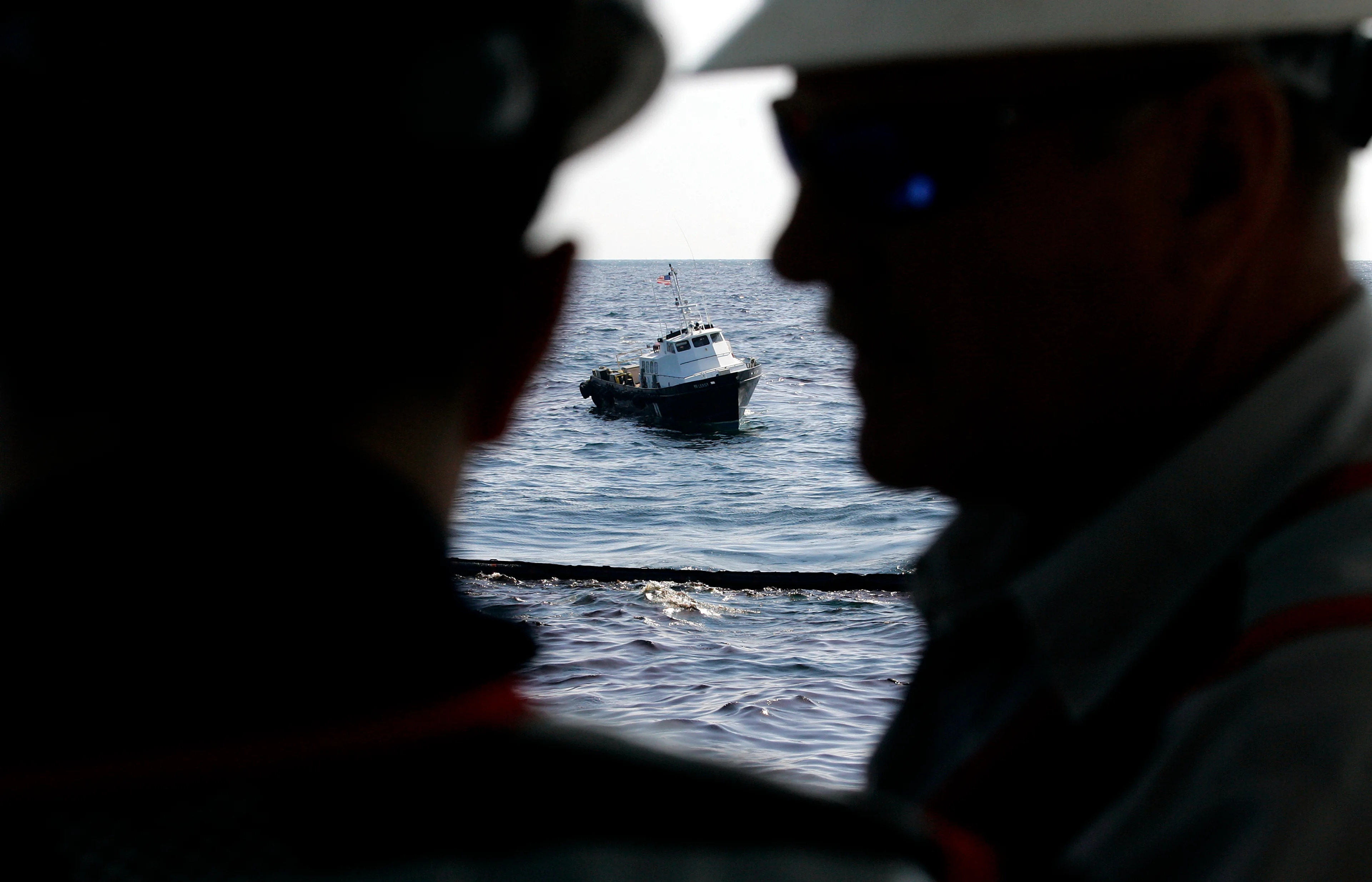 En mannskapsbåt ses i bakgrunnen mens arbeidere om bord på en oljelenser bistår i oppryddingsarbeidet etter Deepwater Horizon-katastrofen i april 2010.