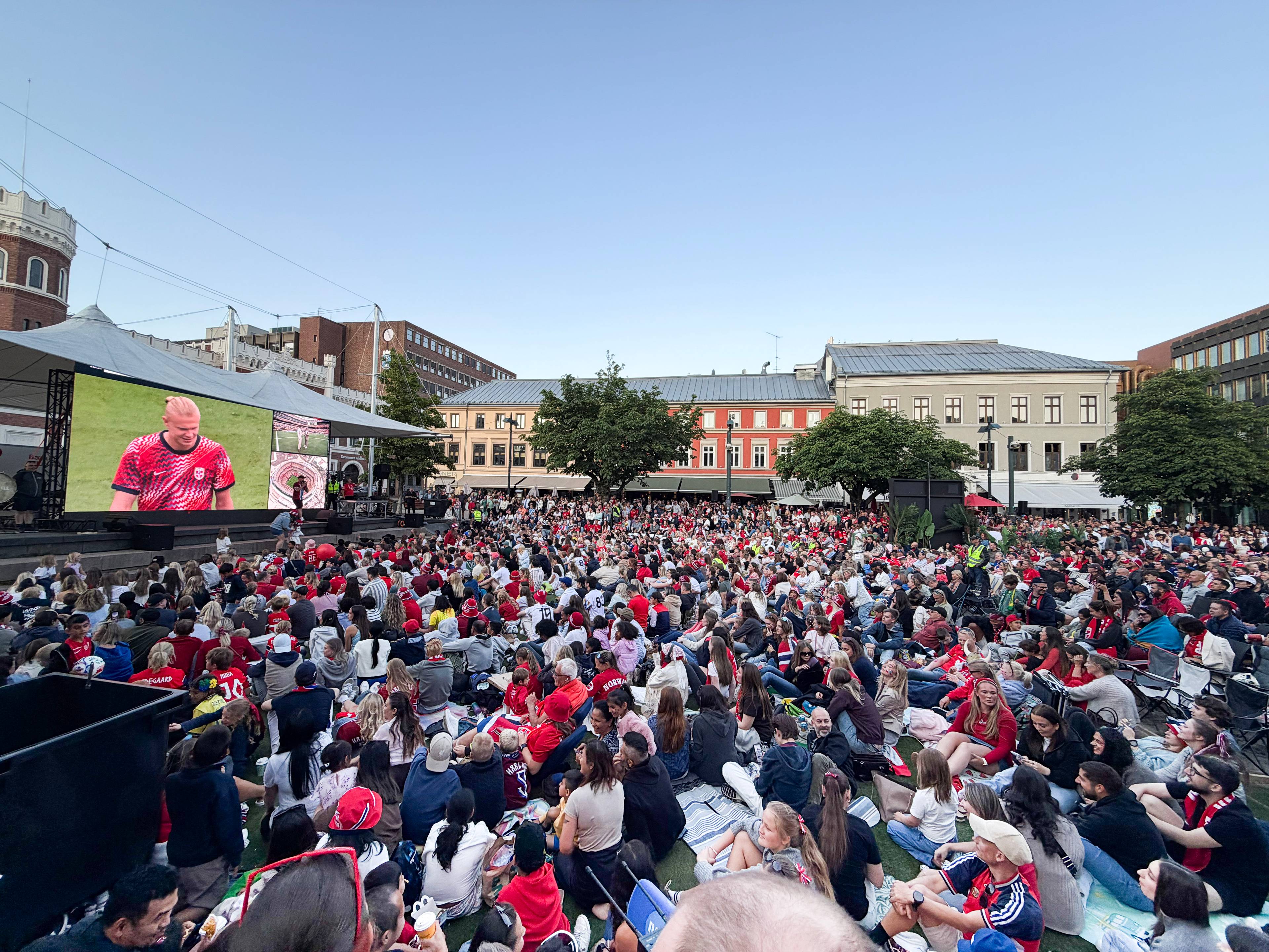 En stor folkemengde samlet foran storskjerm i Drammen. På skjermen vises Erling Braut Haaland. (Bildebeskrivelsen er laget av en KI-tjeneste)