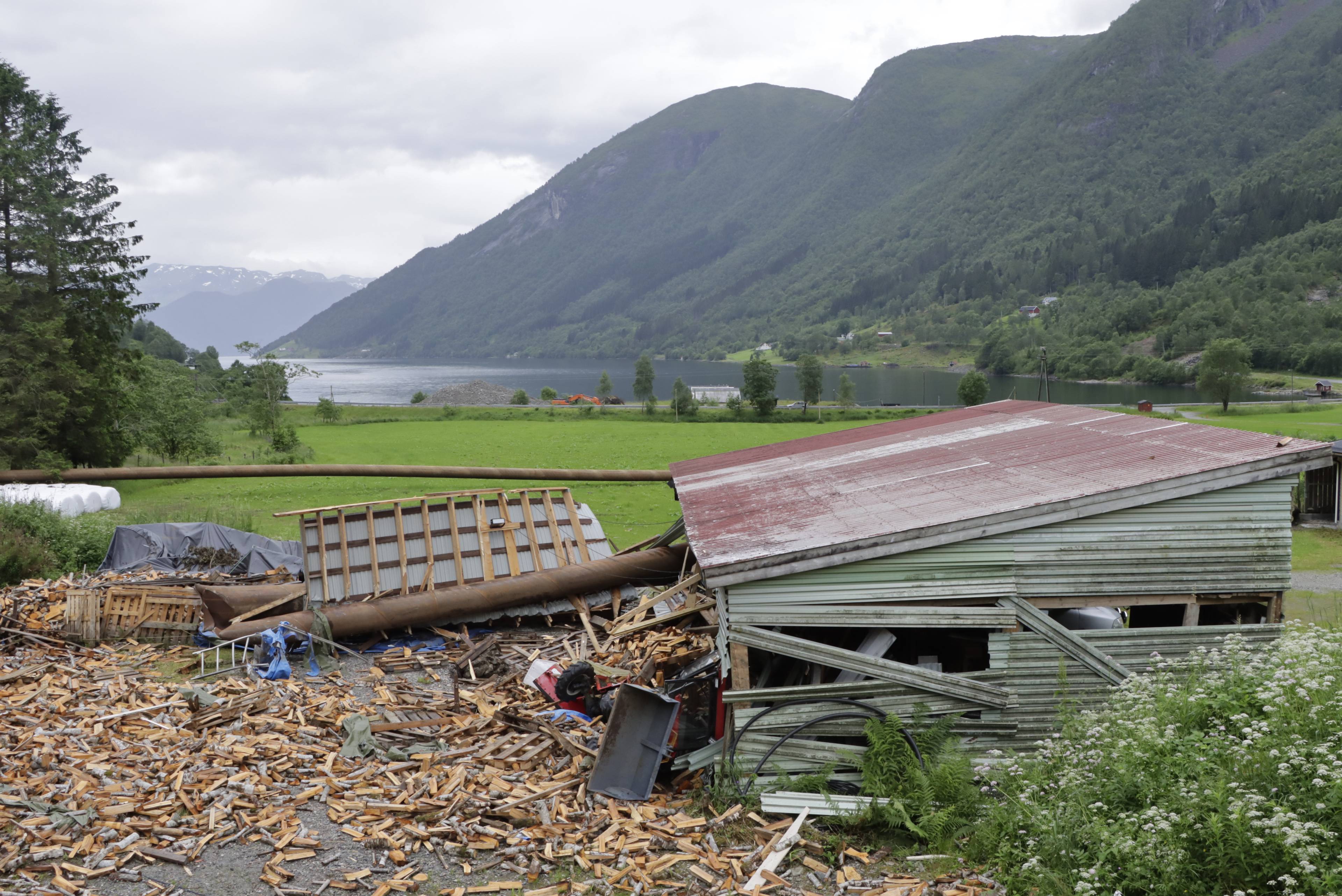 Ødelagt uthus og store mengder ved etter uvær ved en fjord i vestlandsk landskap. (Bildebeskrivelsen er laget av en KI-tjeneste)