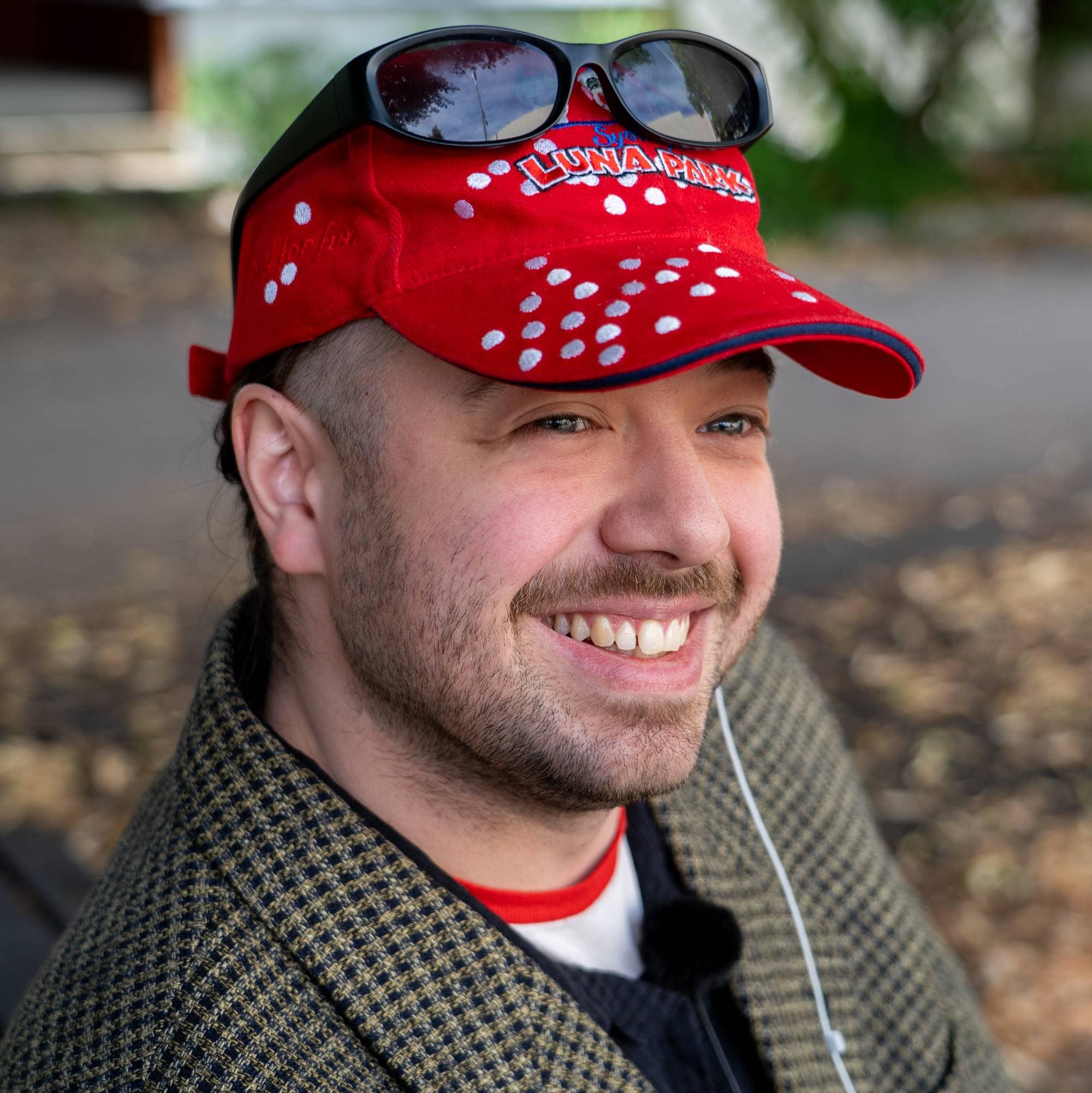 Portrett av en smilende mann med rød caps og solbriller utendørs. (Bildebeskrivelsen er laget av en KI-tjeneste)