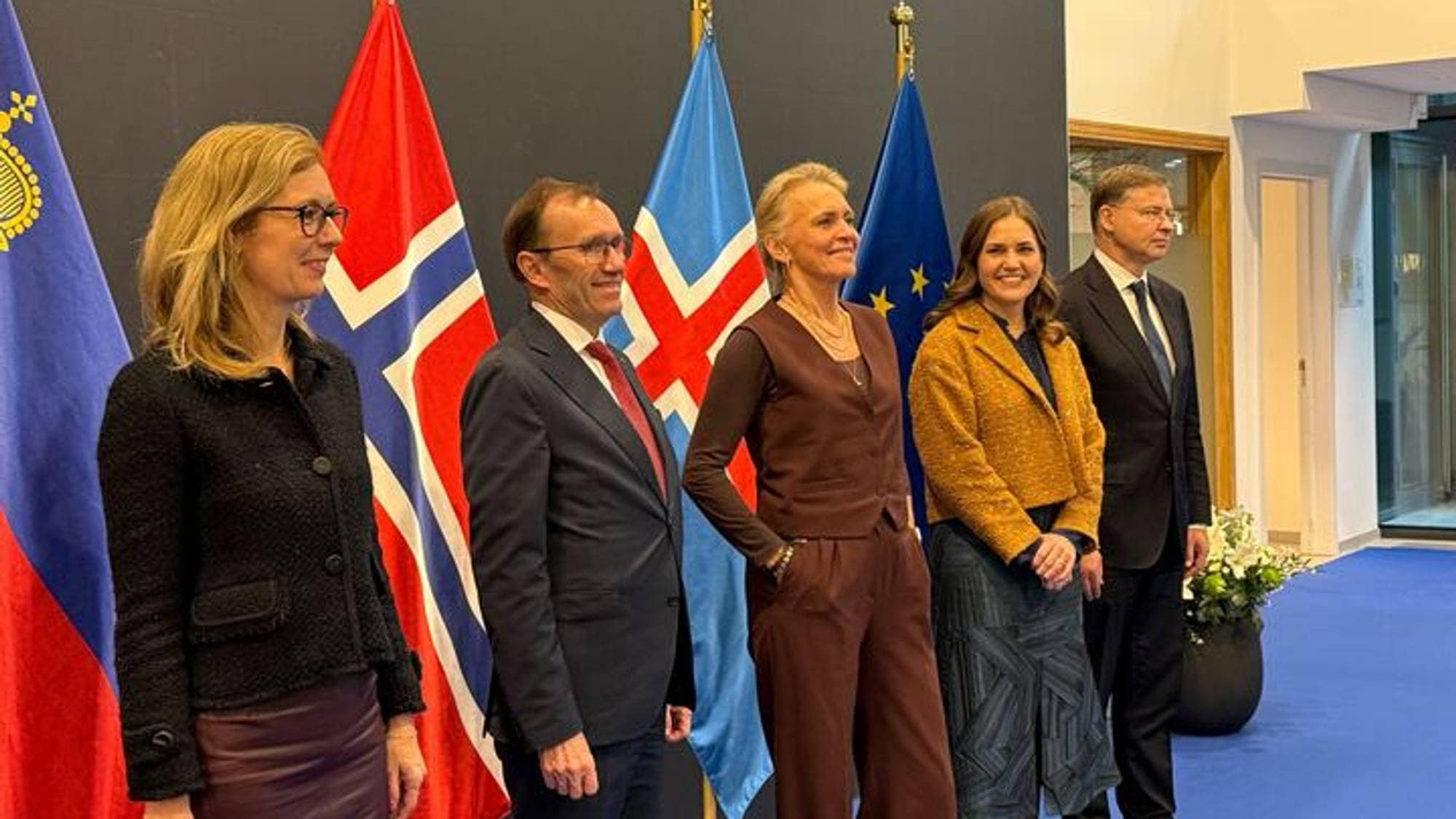 Fem personer i bildet pent kledd, med ulike flagg i bakgrunnen.