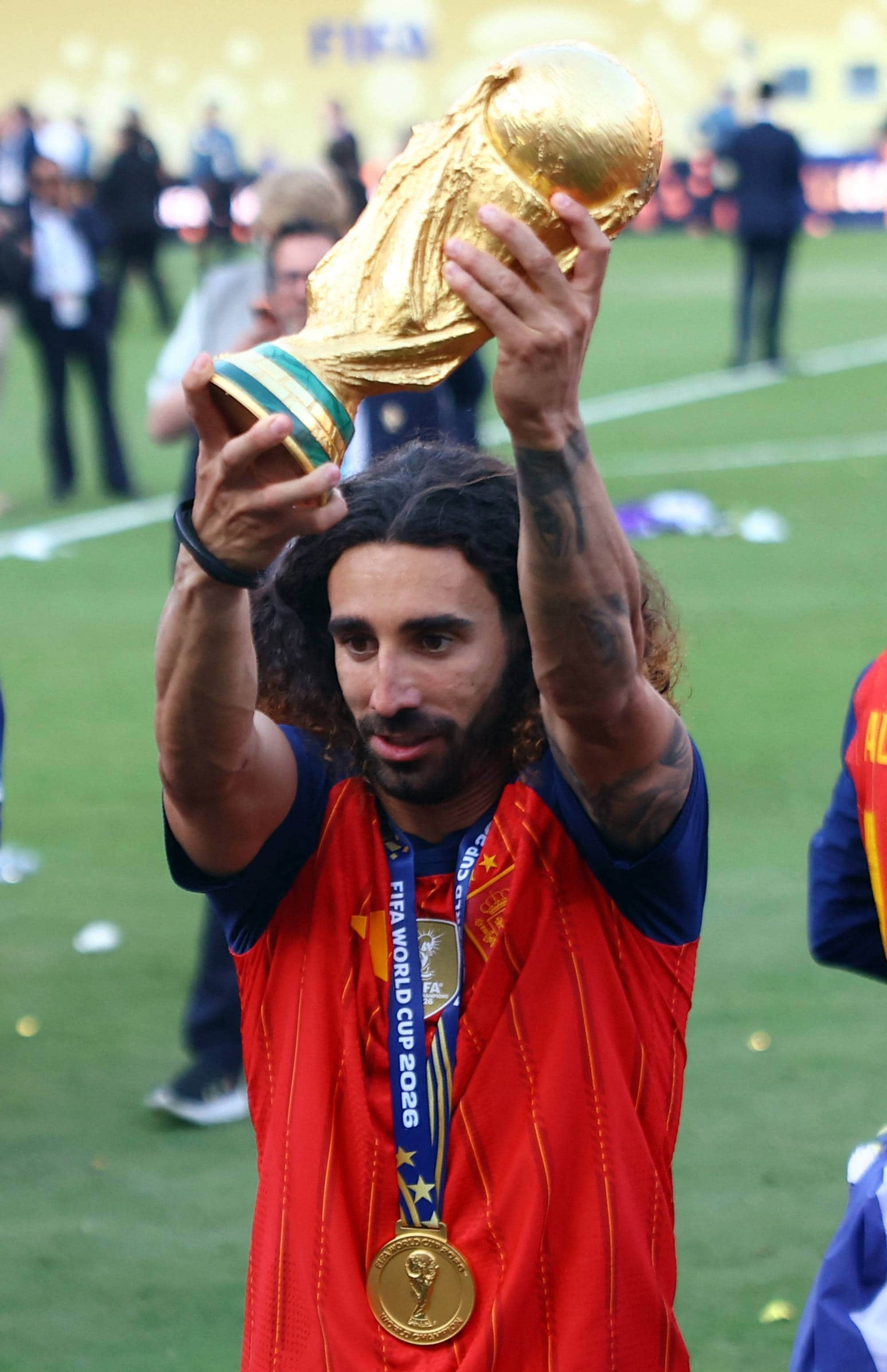 Marc Cucurella løfter VM-trofeet med en gullmedalje rundt halsen på en fotballbane. (Bildebeskrivelsen er laget av en KI-tjeneste)